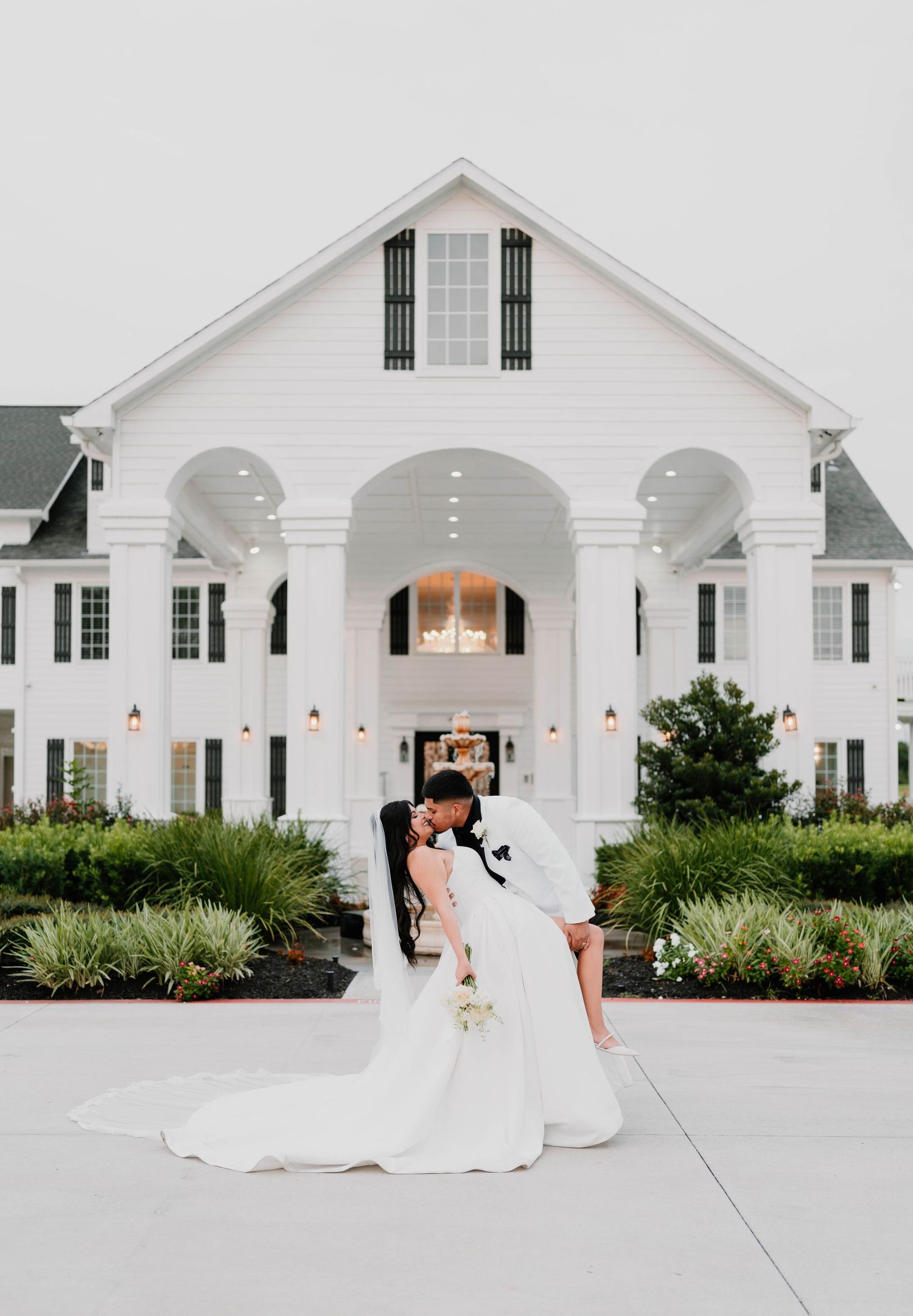 A stunning white wedding venue with elegant columns and arches creates a romantic backdrop for a bridal photoshoot.