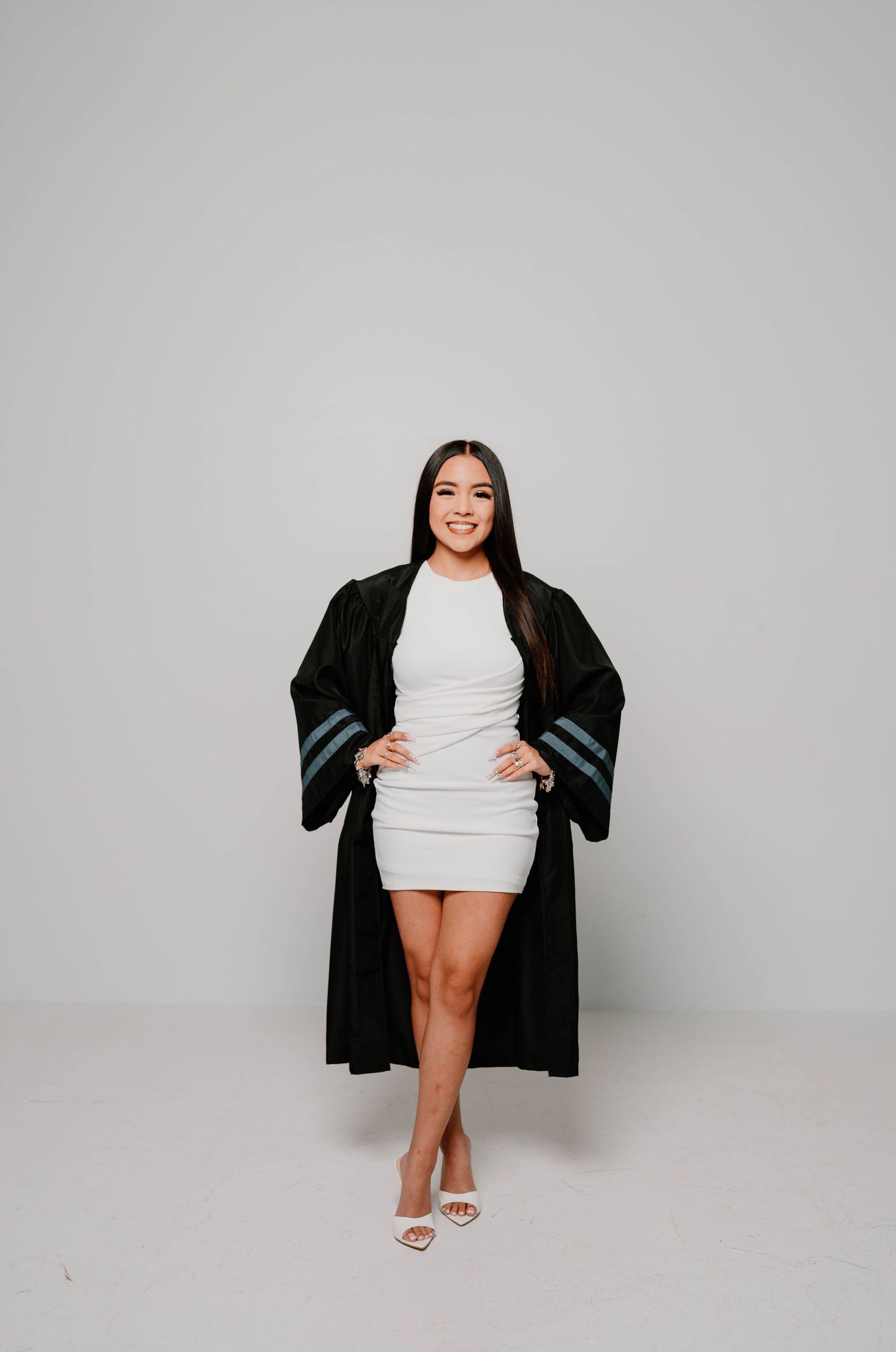 Studio graduation portraits in white dress and black gown against grey backdrop.