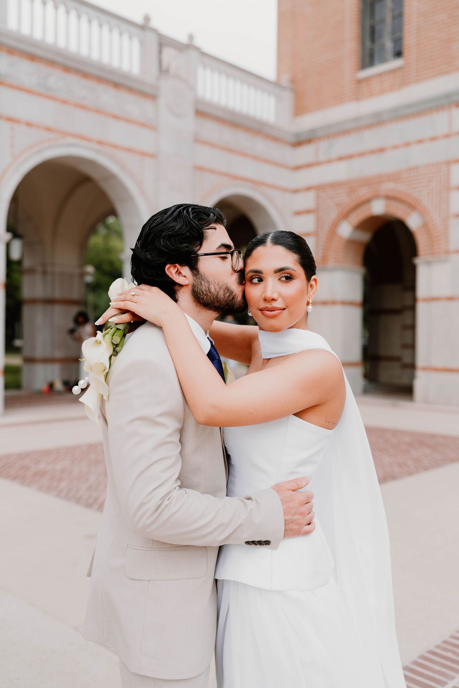 Romantic wedding couple embraces in an elegant archway courtyard setting.