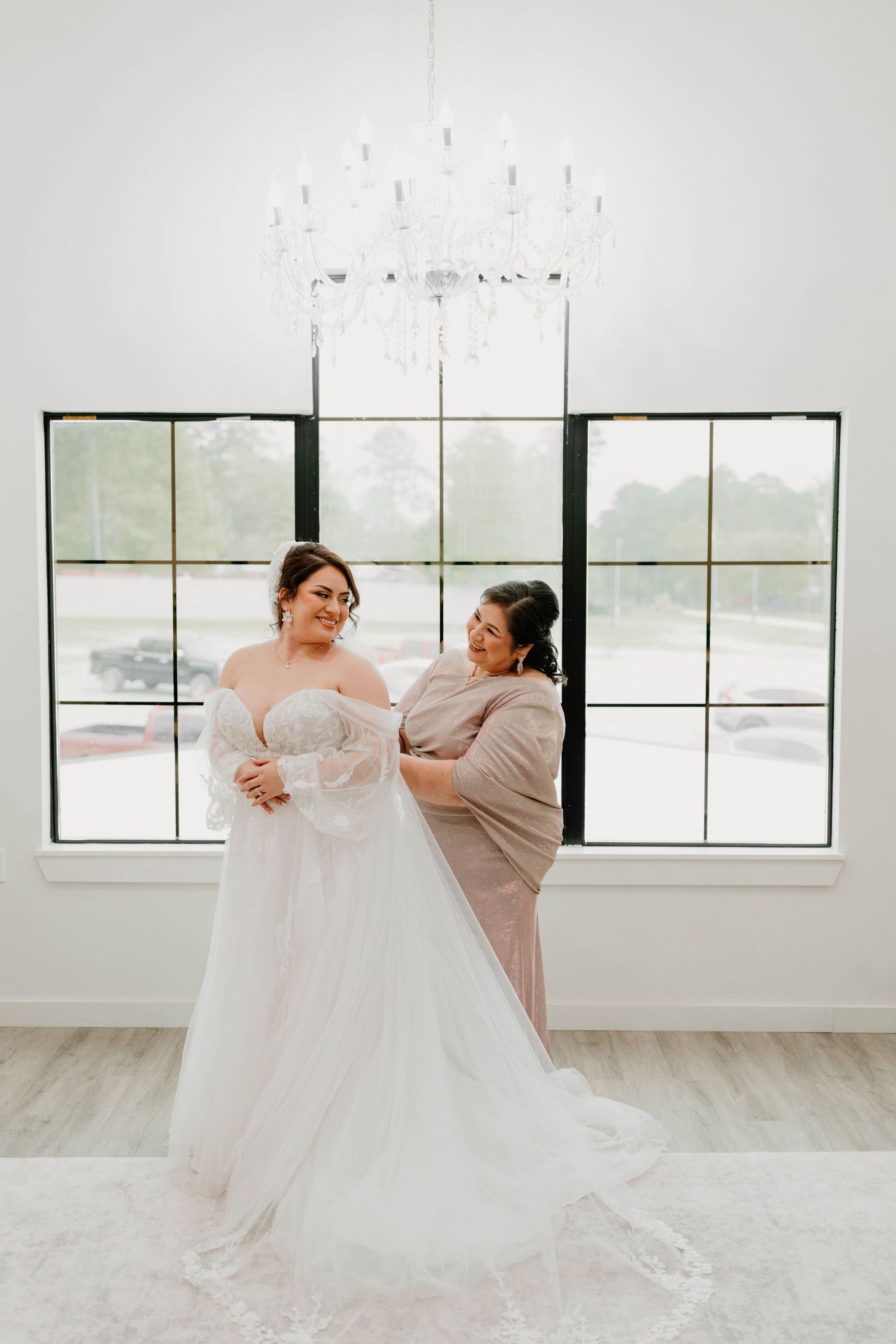 A bride in a flowing white gown twirls gracefully in a bright room with large windows.