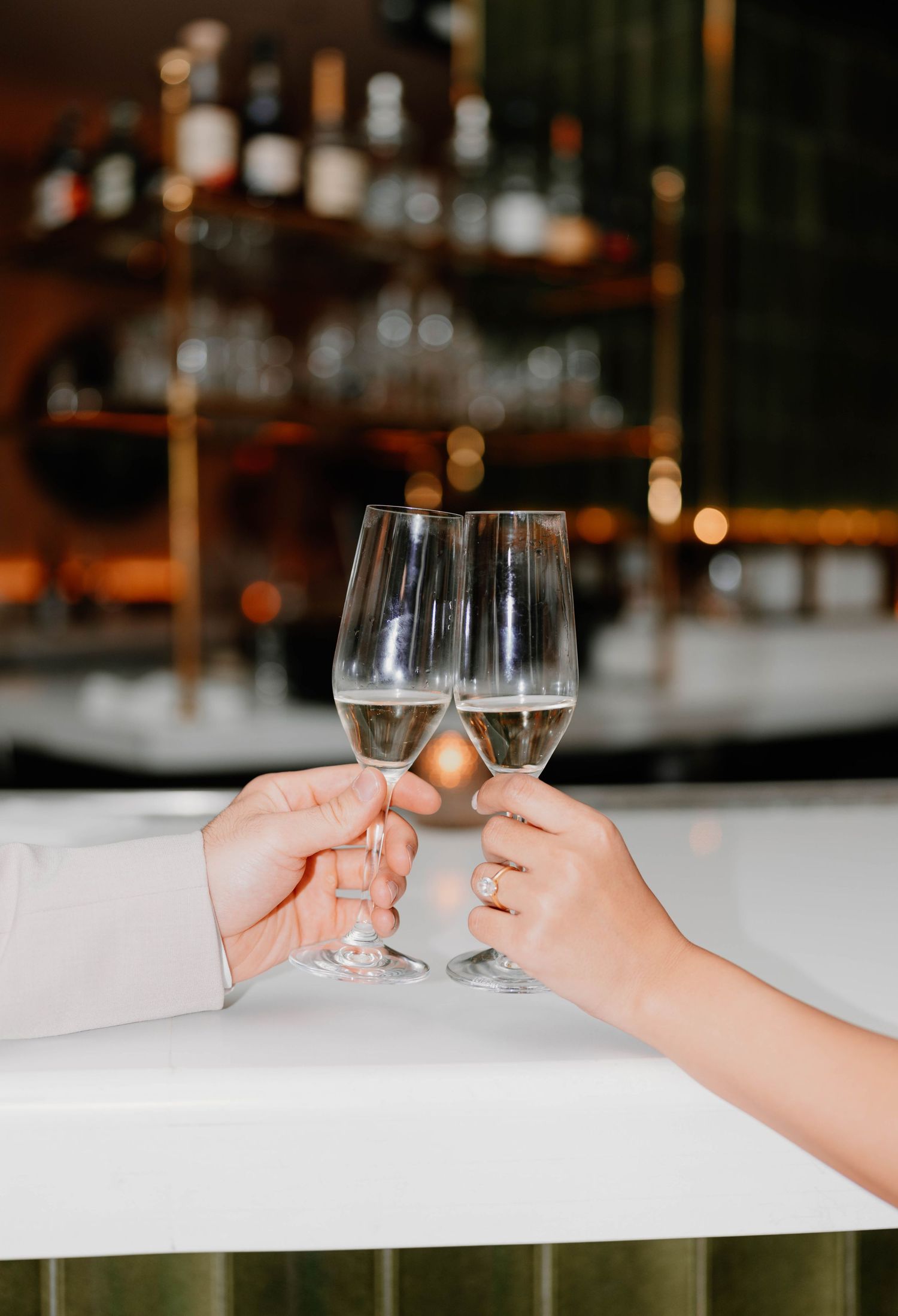 Two hands clink wine glasses together in romantic toast at bar.