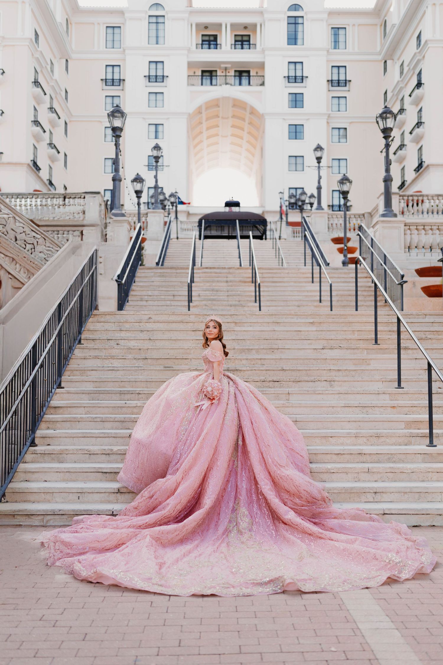 Pink ballgown dress spreads dramatically across grand marble staircase.