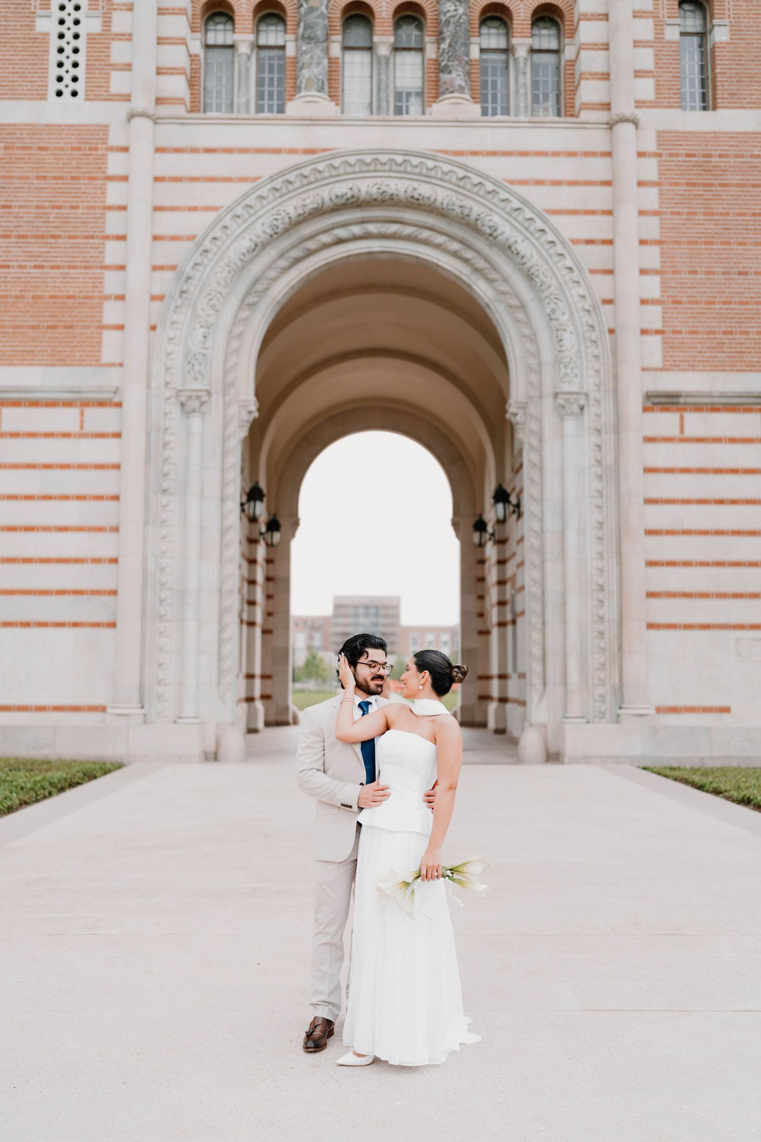 Wedding couple photographed in front of a grand architectural archway with pink brick details.