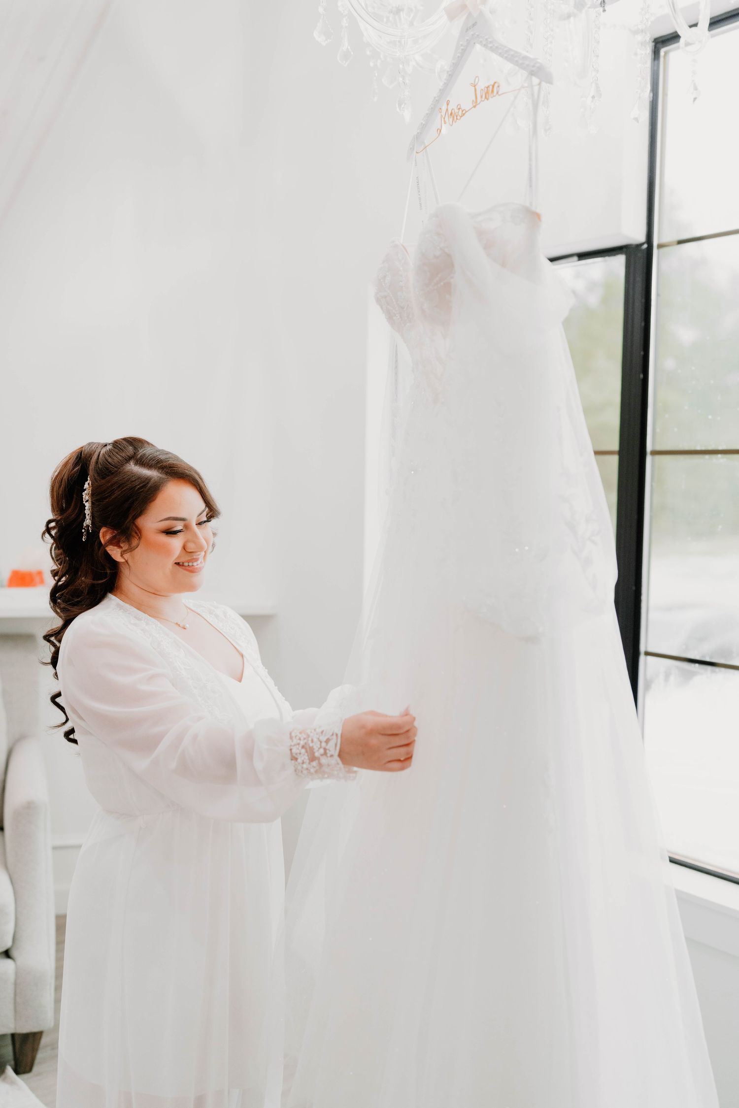 Preparation scene with white wedding dress hanging in bright modern room.