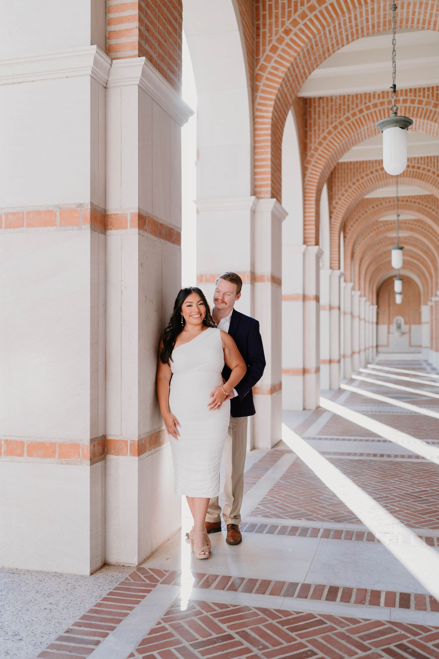 A couple poses together in an elegant arched hallway with terracotta and white architectural details.