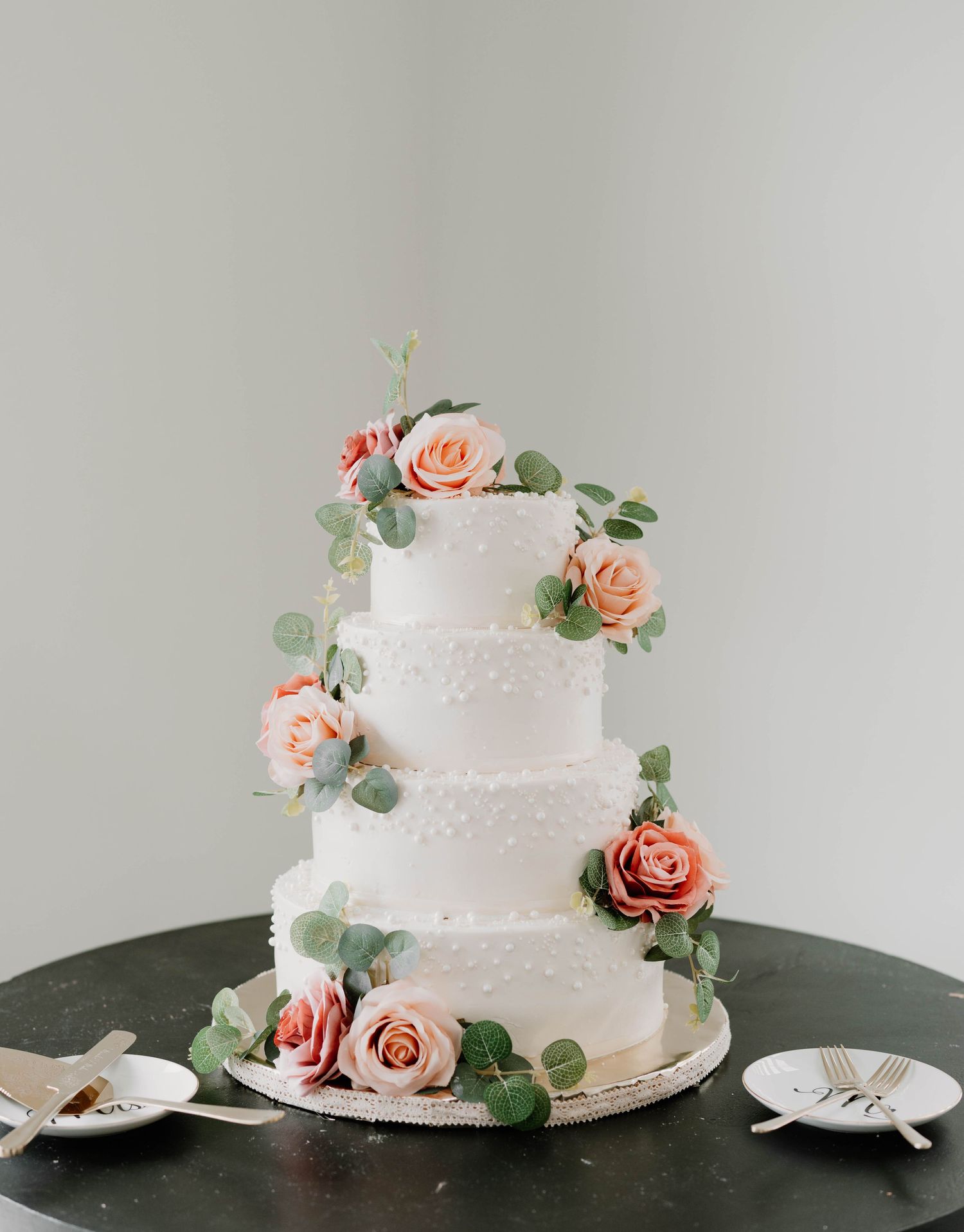 Elegant white wedding cake with pearl details and peach roses on dark surface.