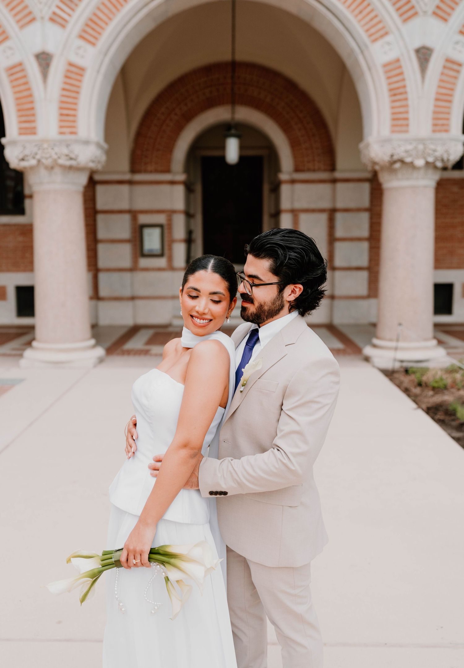 Wedding couple dances playfully in an ornate courtyard with arched columns.