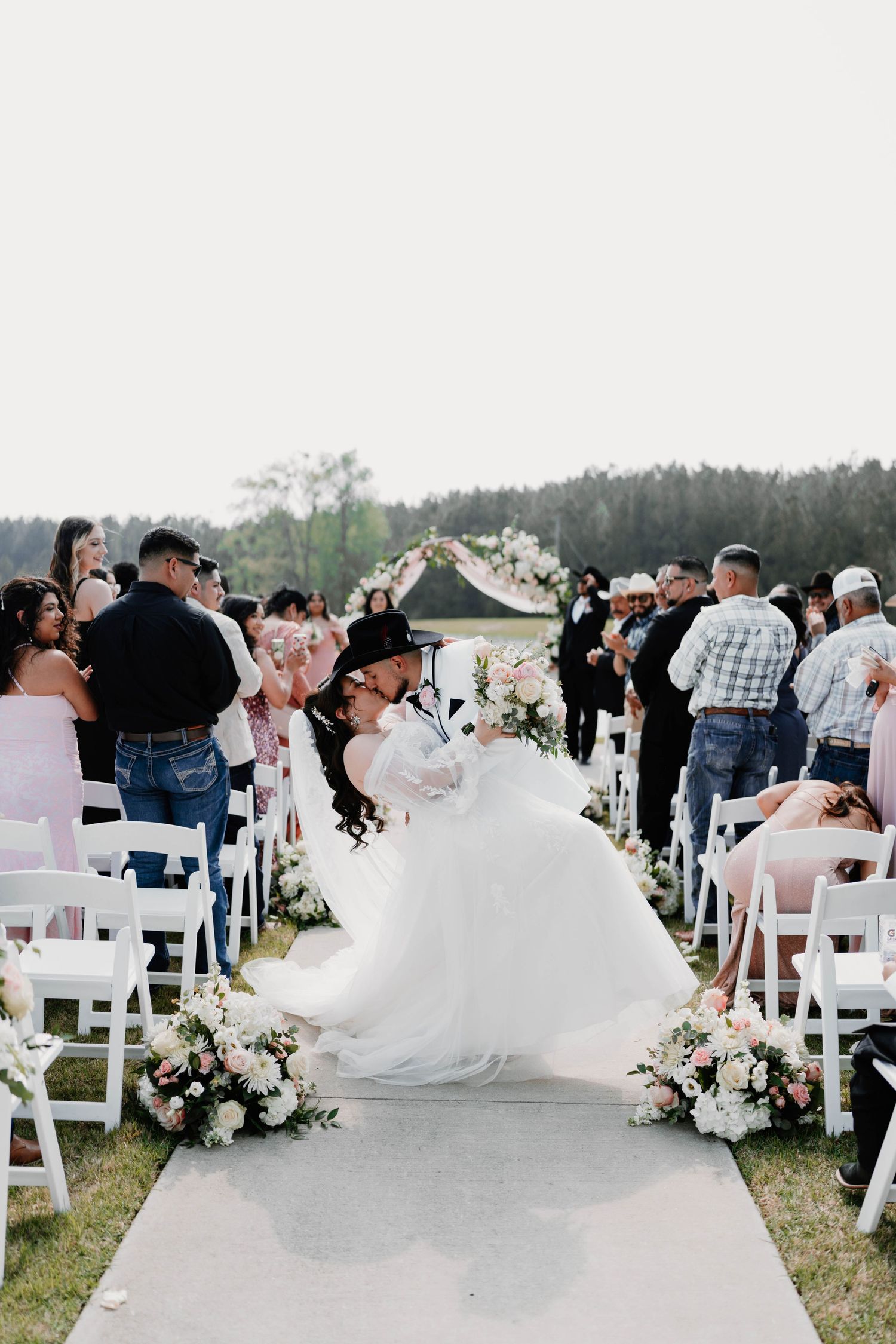 Outdoor wedding ceremony setup with white chairs and floral arrangements along the aisle.