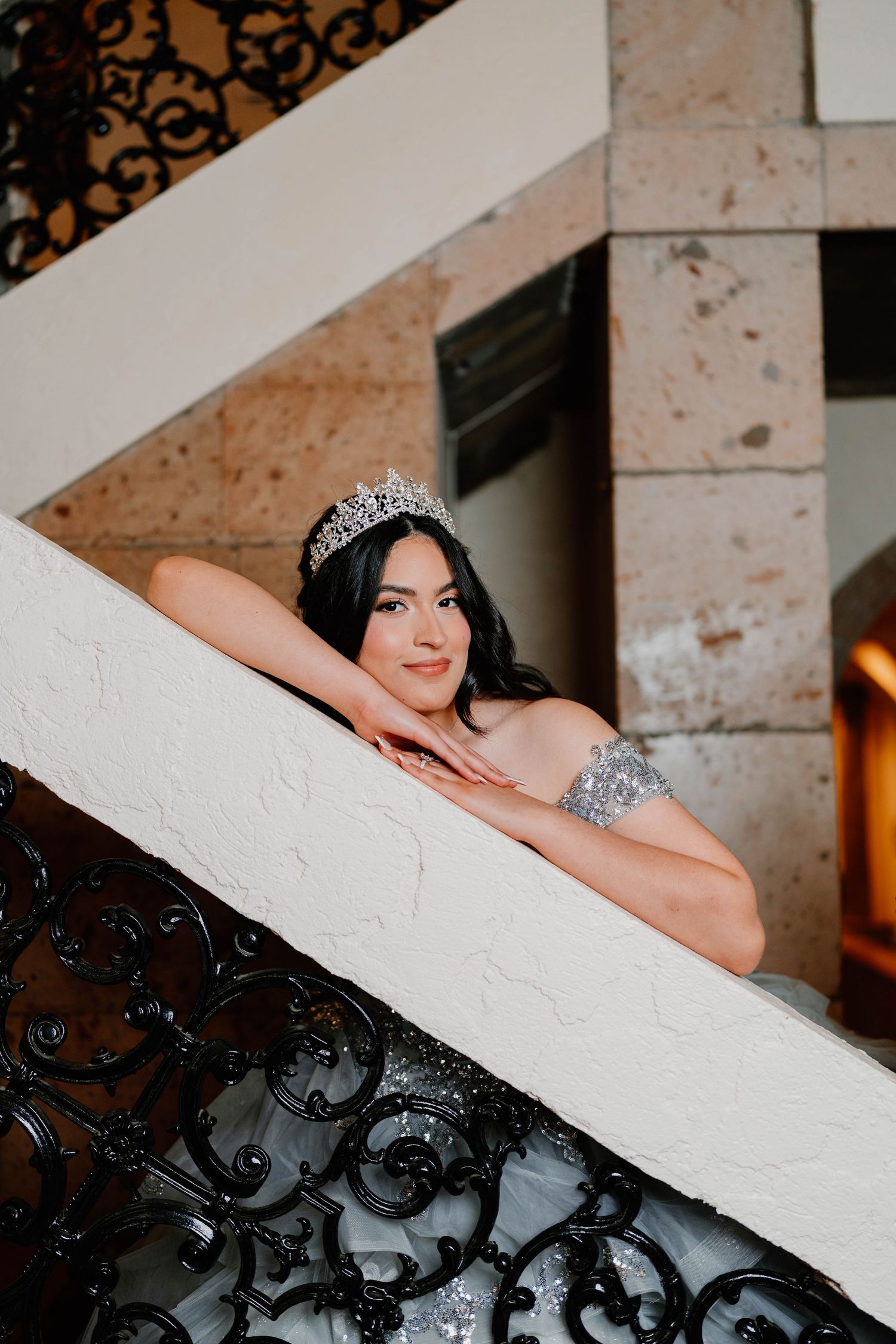 Elegant pose on white staircase with ornate black iron railing details.