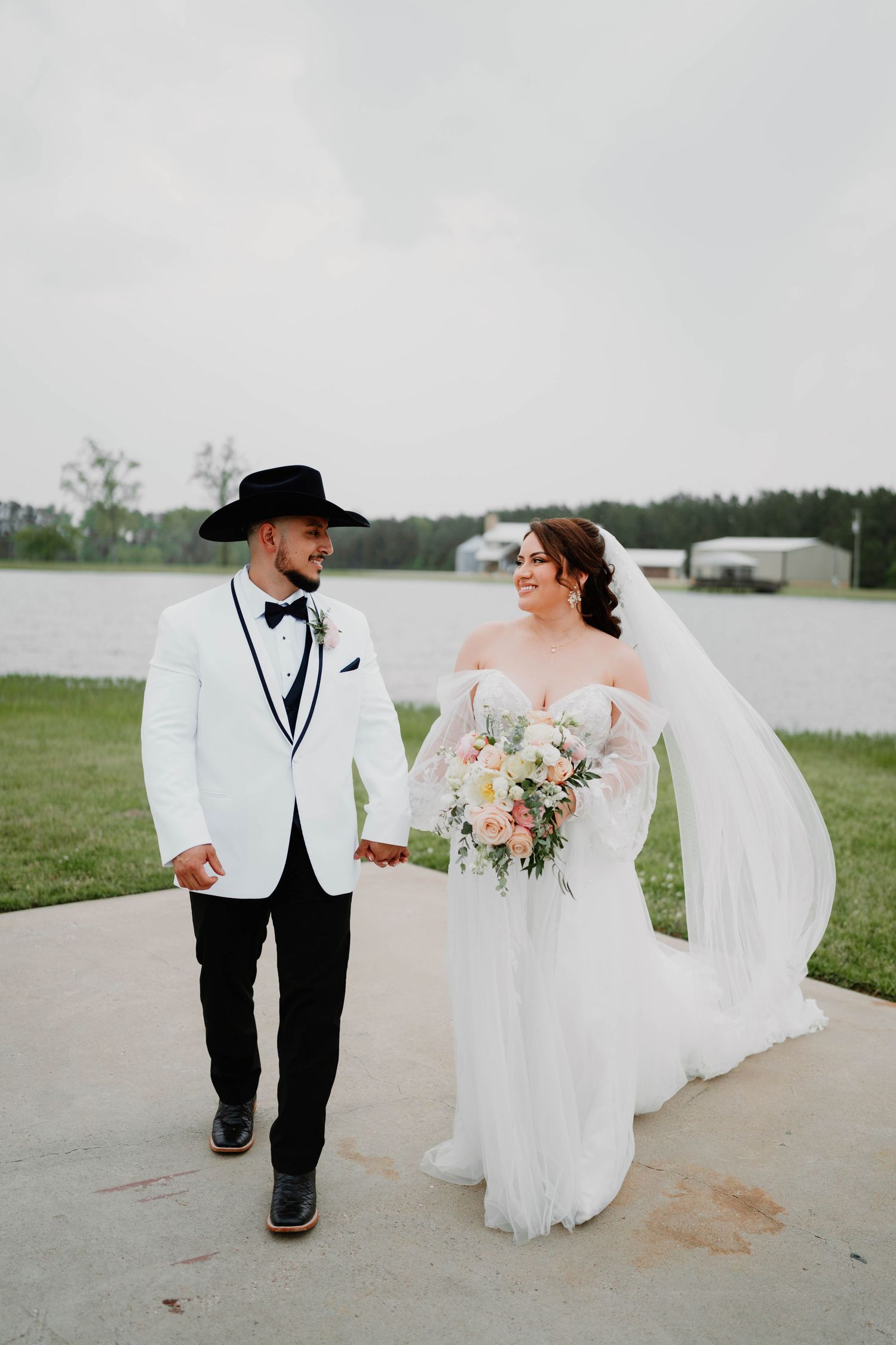 A couple walks hand in hand across a grassy field during their wedding photoshoot.