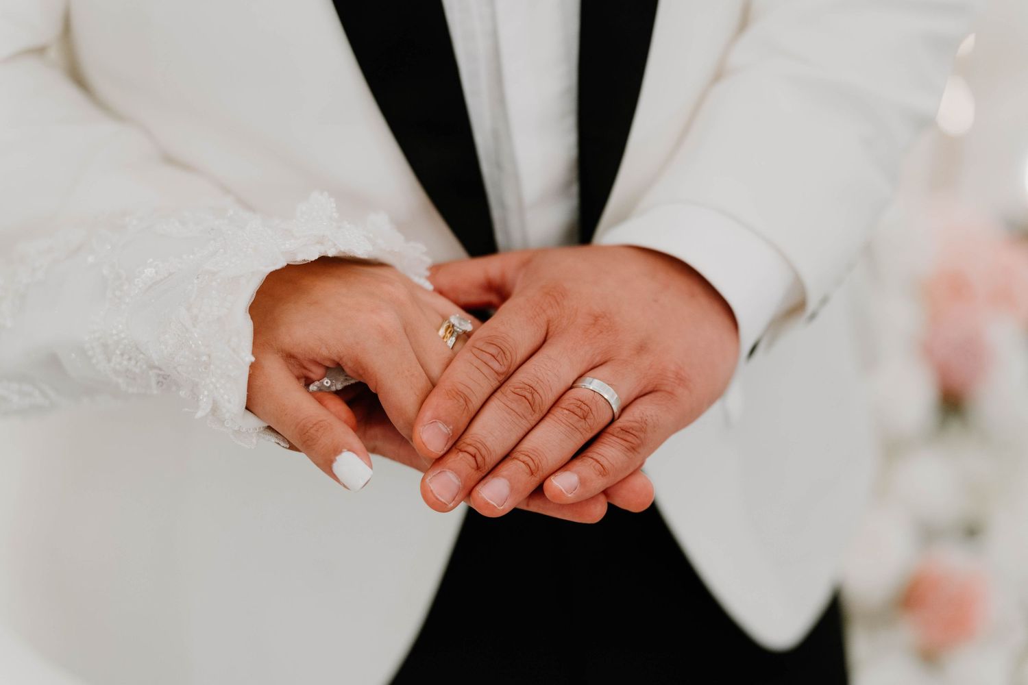 Close-up of hands with wedding rings against a black and white formal attire background.