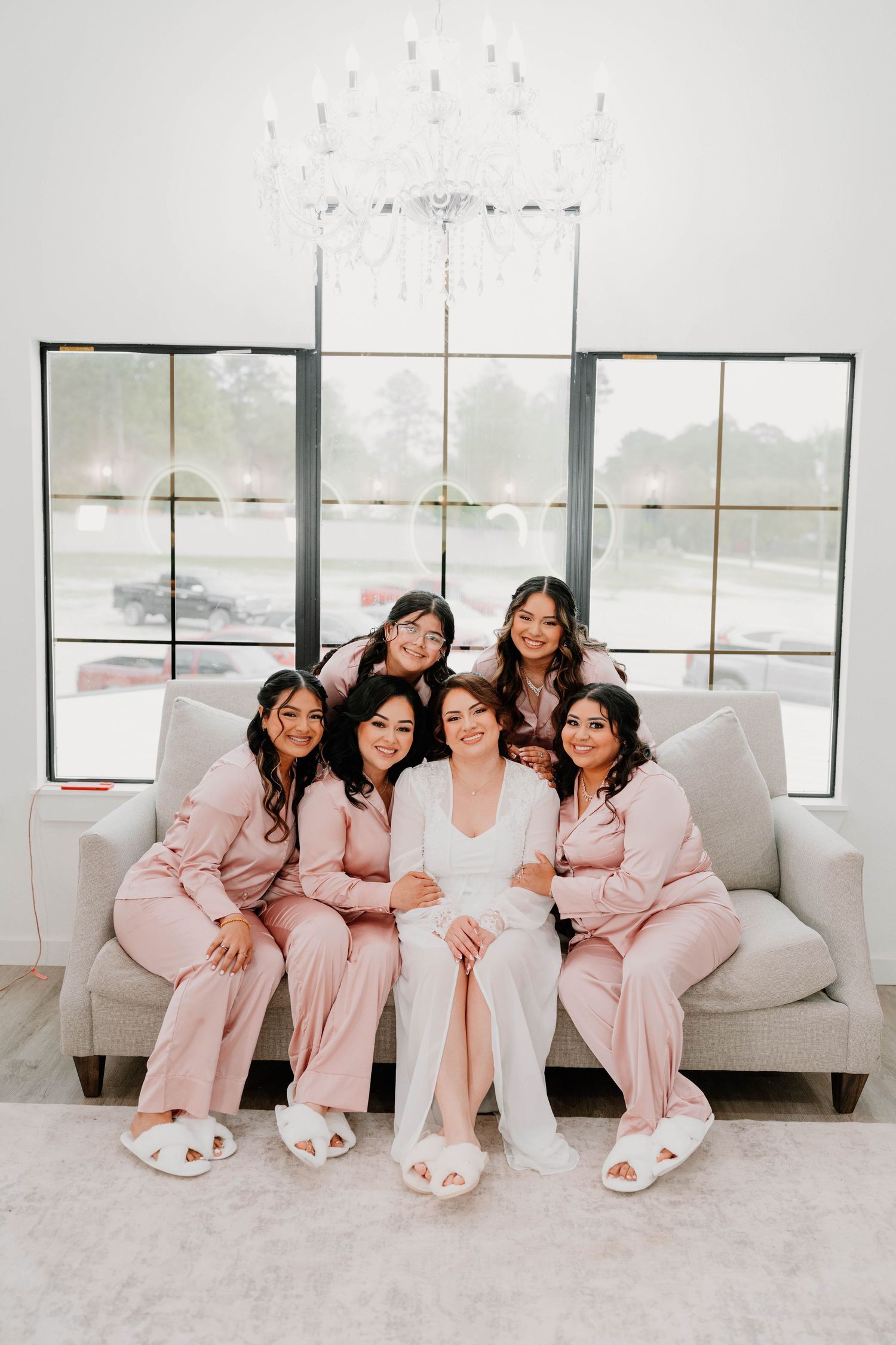 Bridesmaids in matching pink pajamas relaxing on white couch.