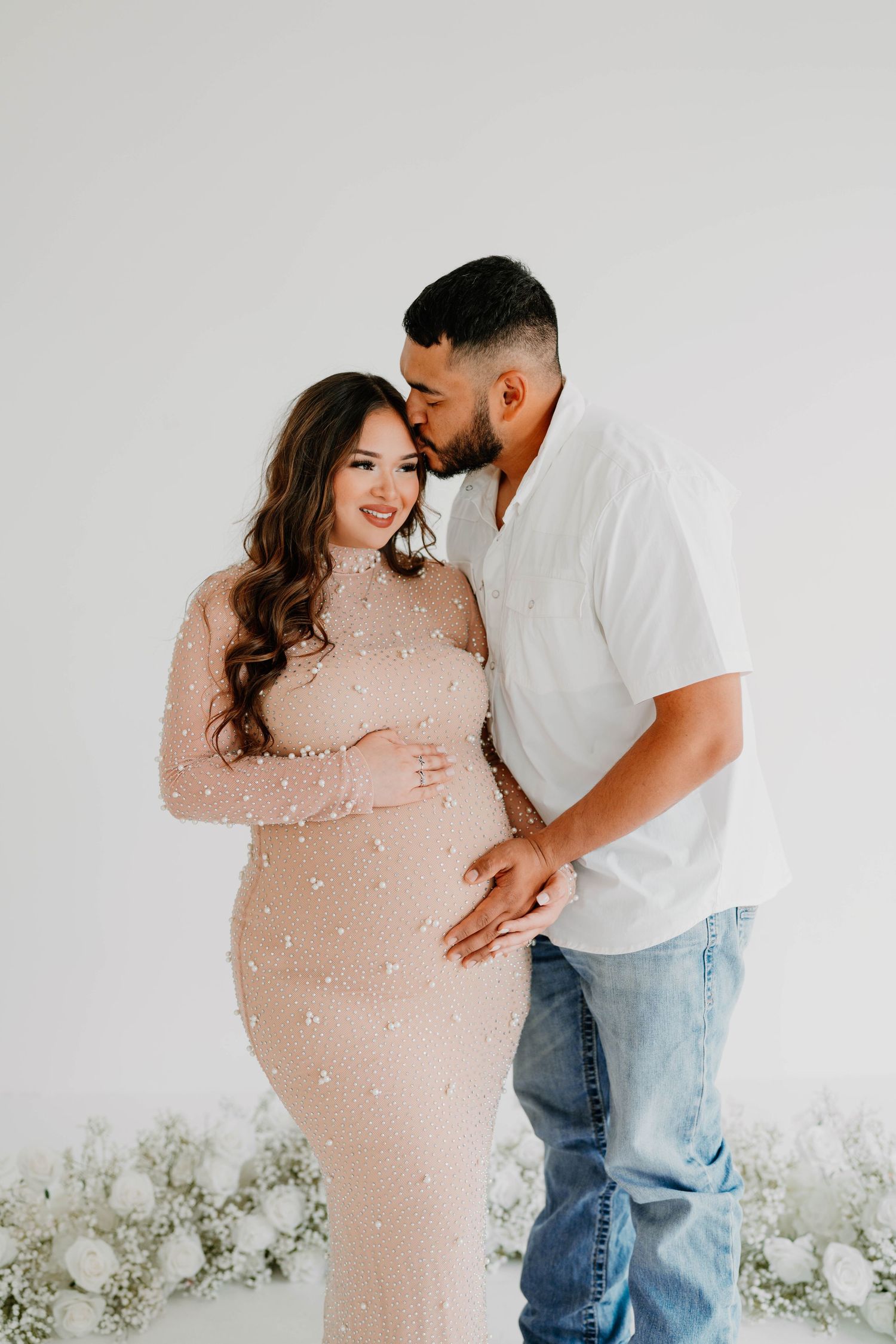 Intimate maternity session with couple in white studio setting.