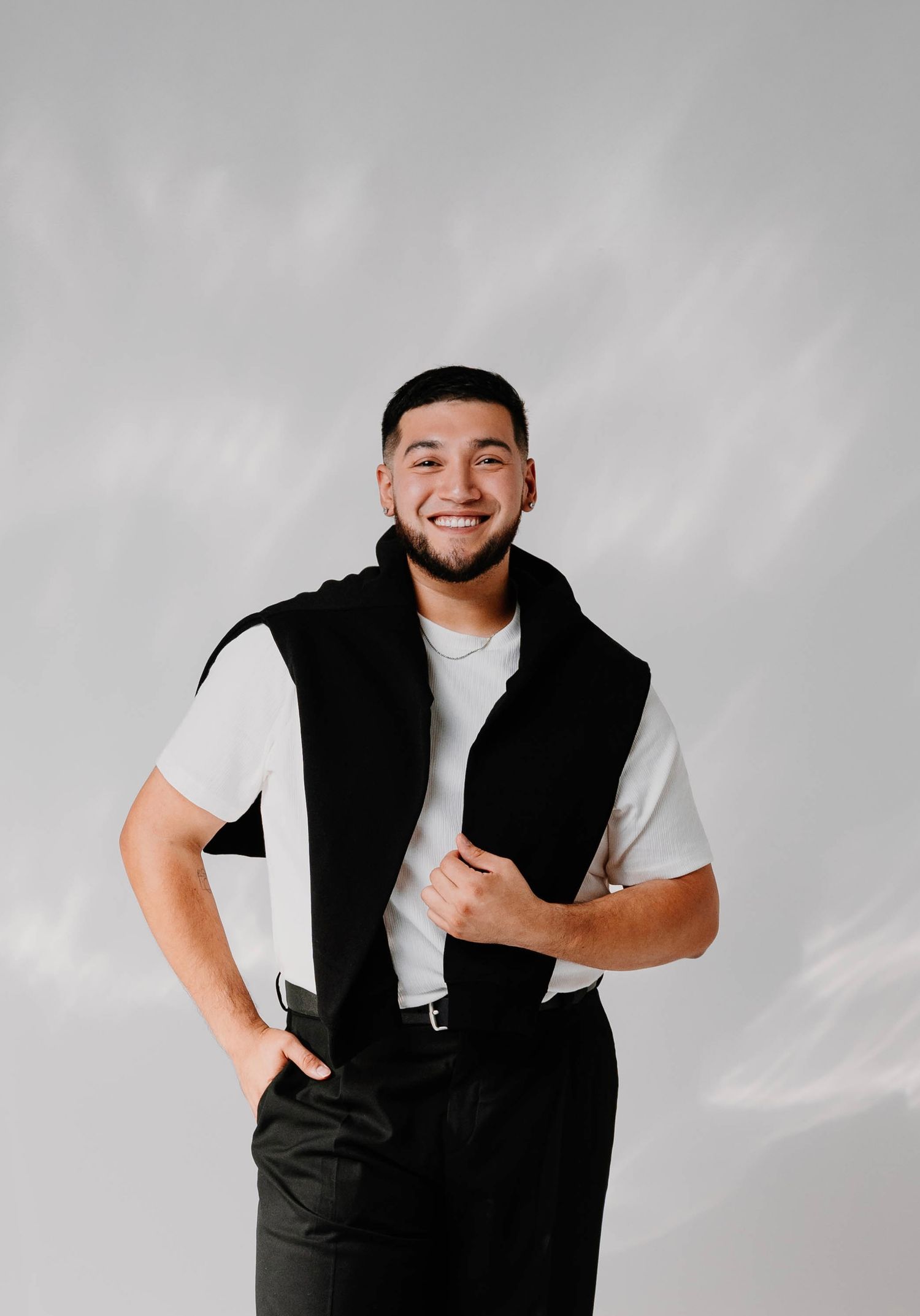 A person in a black vest and white t-shirt poses expressively against a gray background in a photo series.