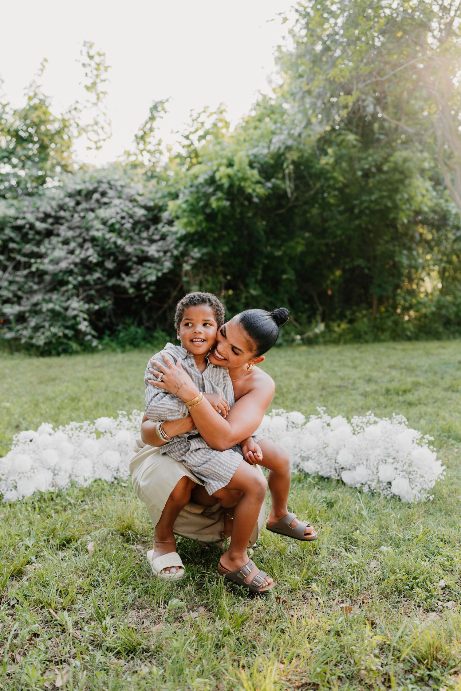 Tender family moment captured in sunlit garden with white floral elements.