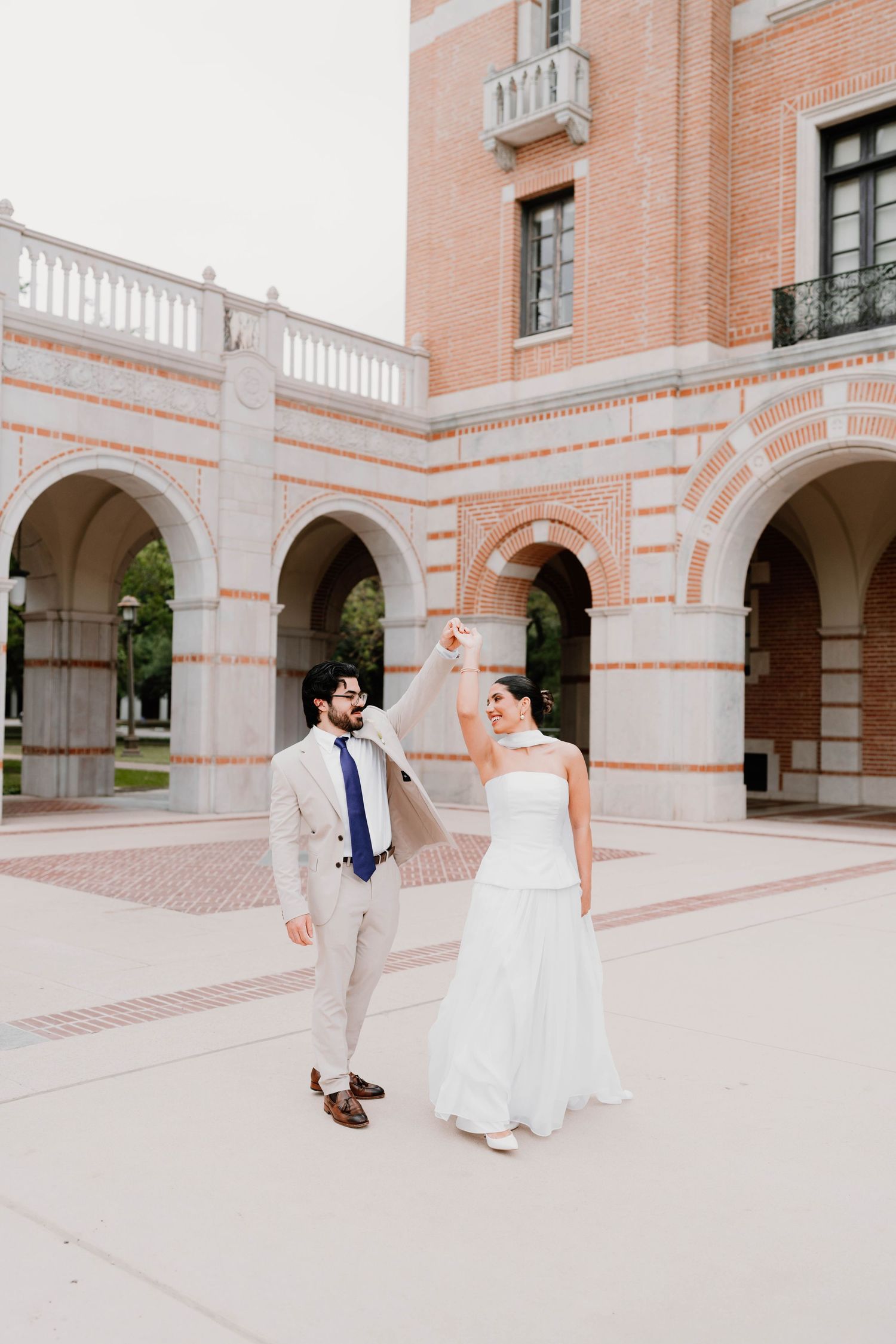 Elegant wedding couple walking along a beautiful pink brick colonnade.