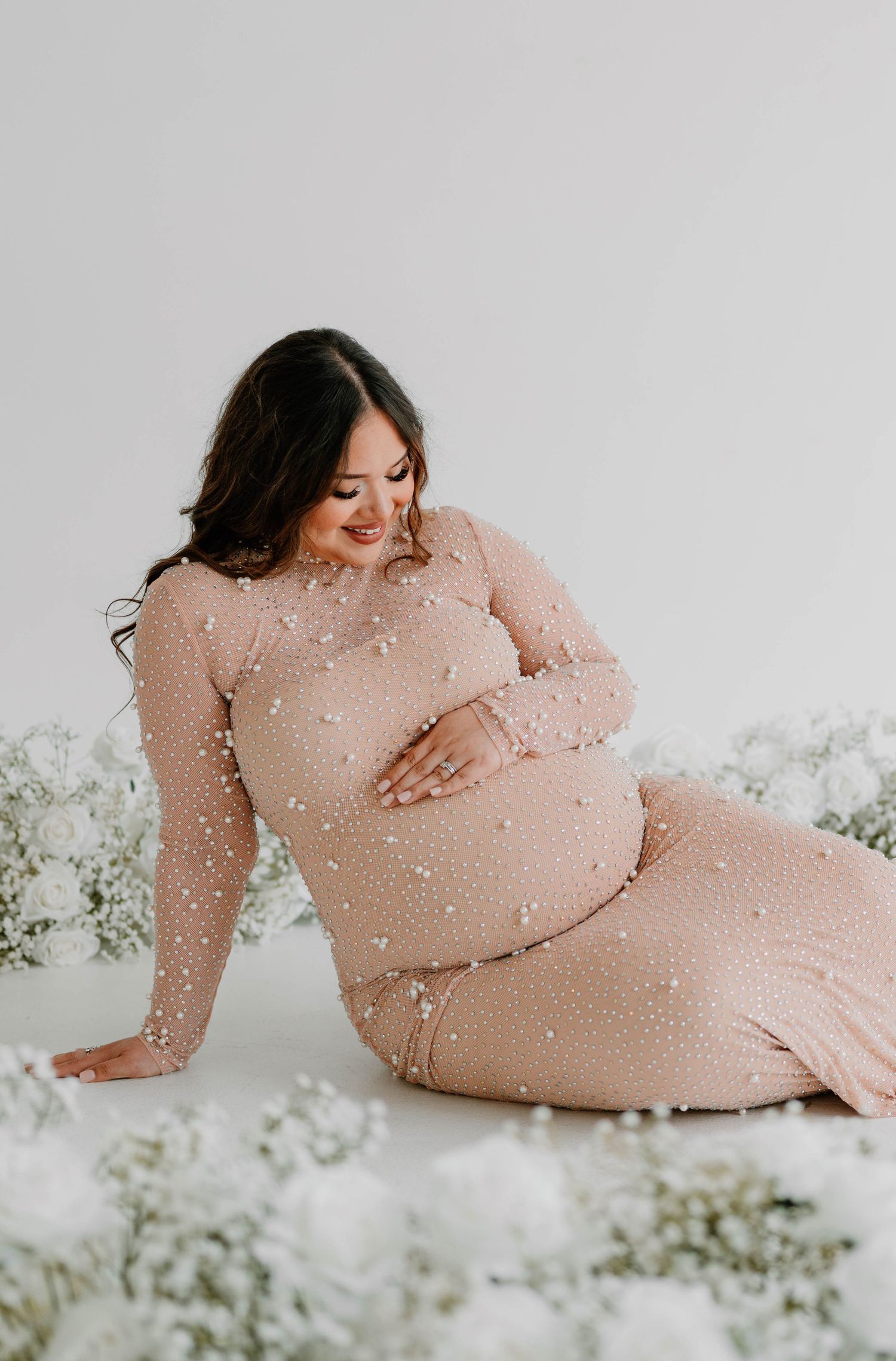 Artistic maternity photo shoot with soft pink tones and white floral elements creating a dreamy atmosphere.