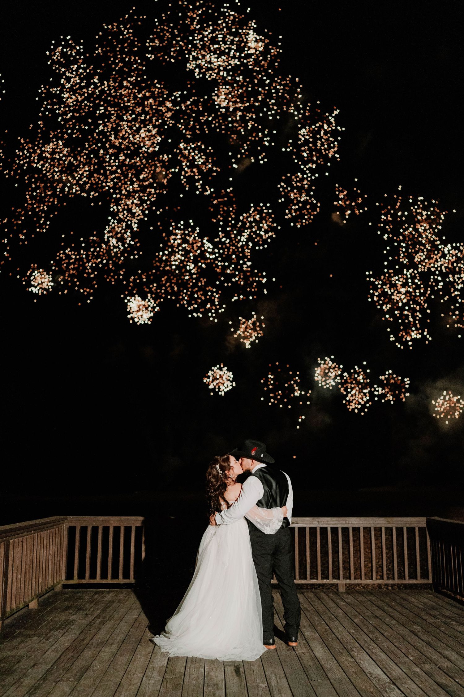 A romantic moment under twinkling lights on a wooden deck during a nighttime wedding celebration.
