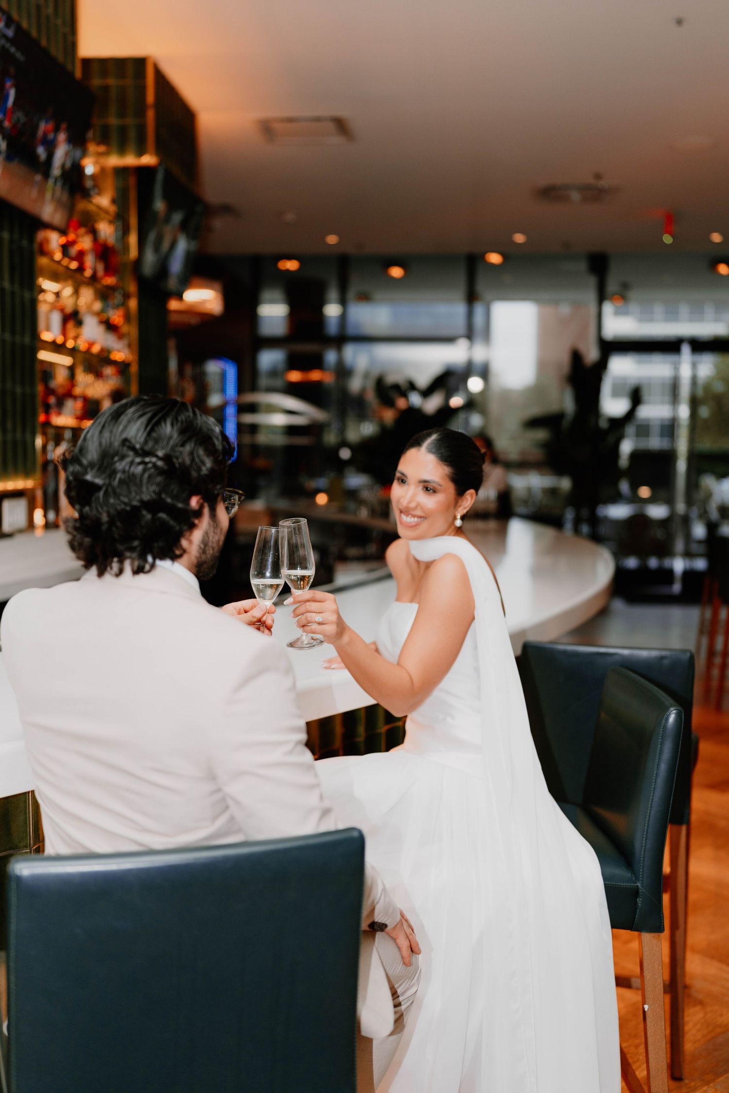 Couple shares intimate moment while toasting with wine glasses at a bar.