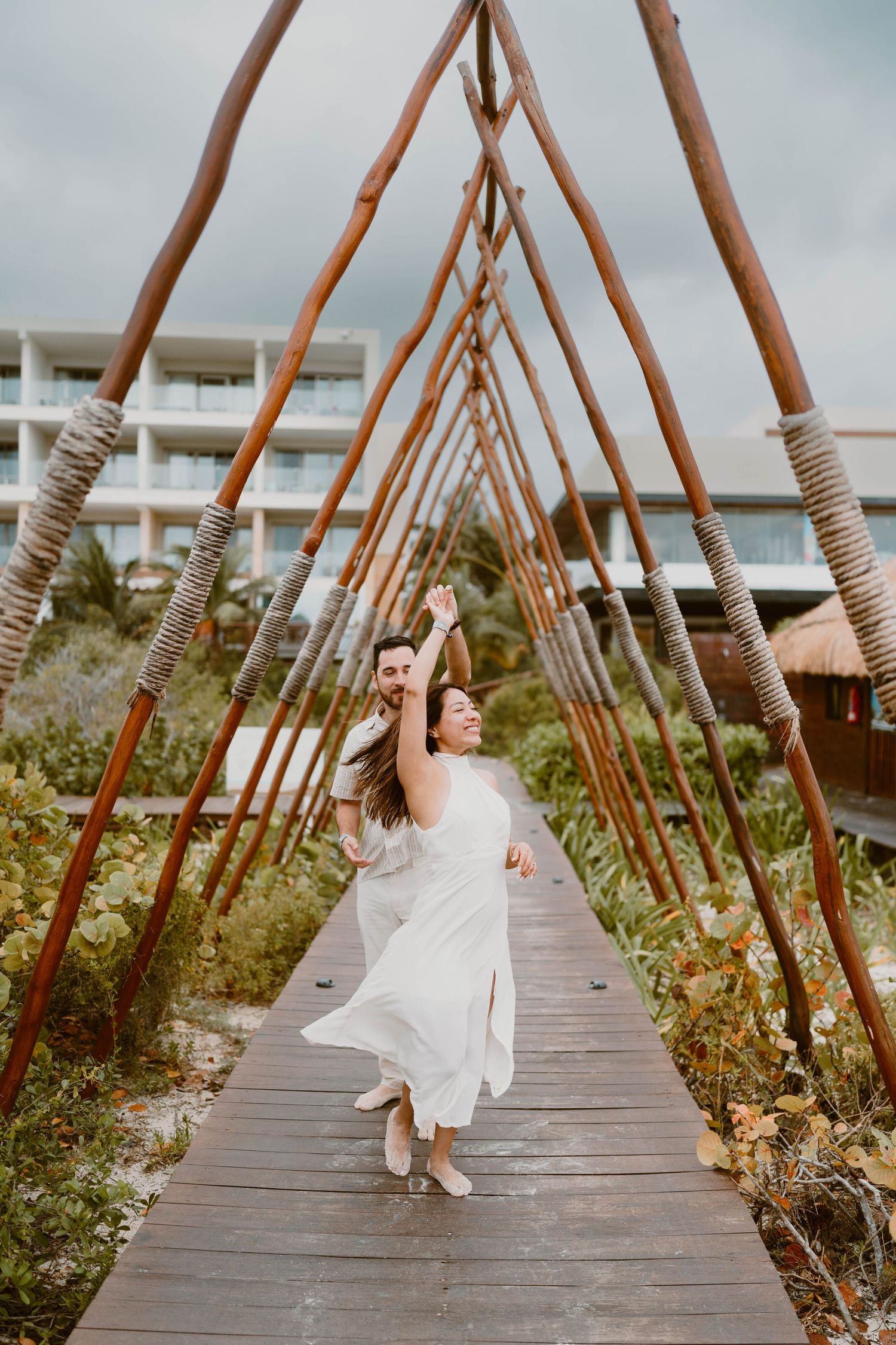 Artistic sequence of couple walking along wooden pathway with rope-lined posts.