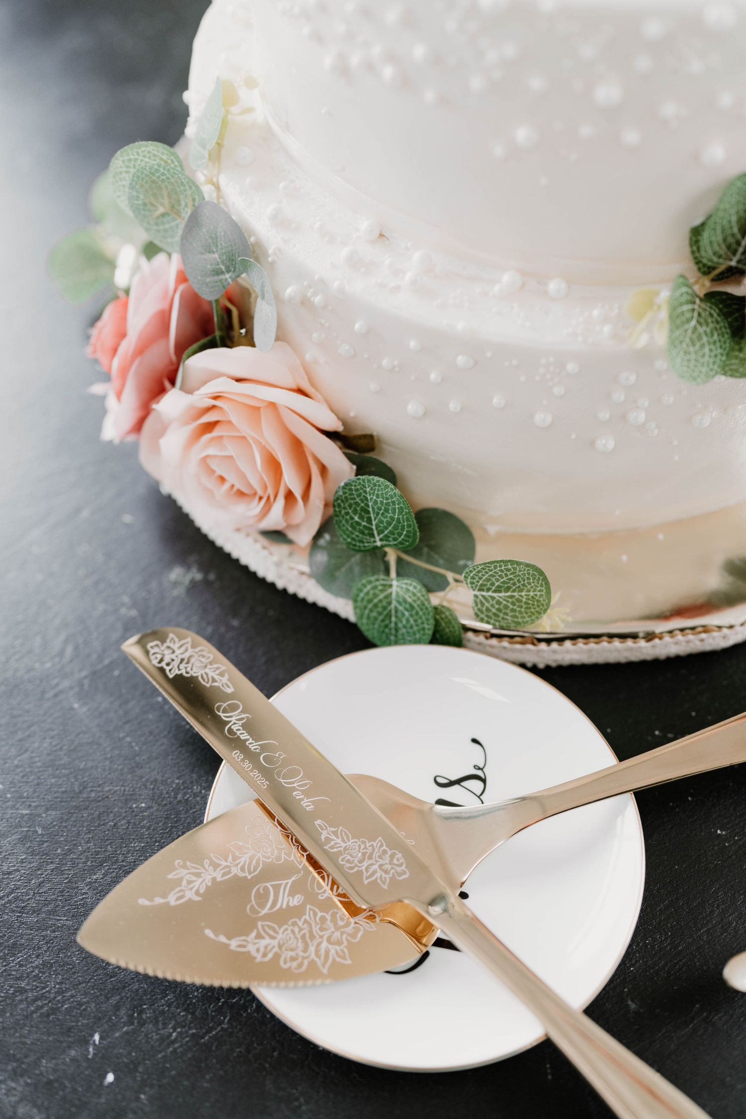 Ornate cake cutting set with decorative handles beside white wedding cake.
