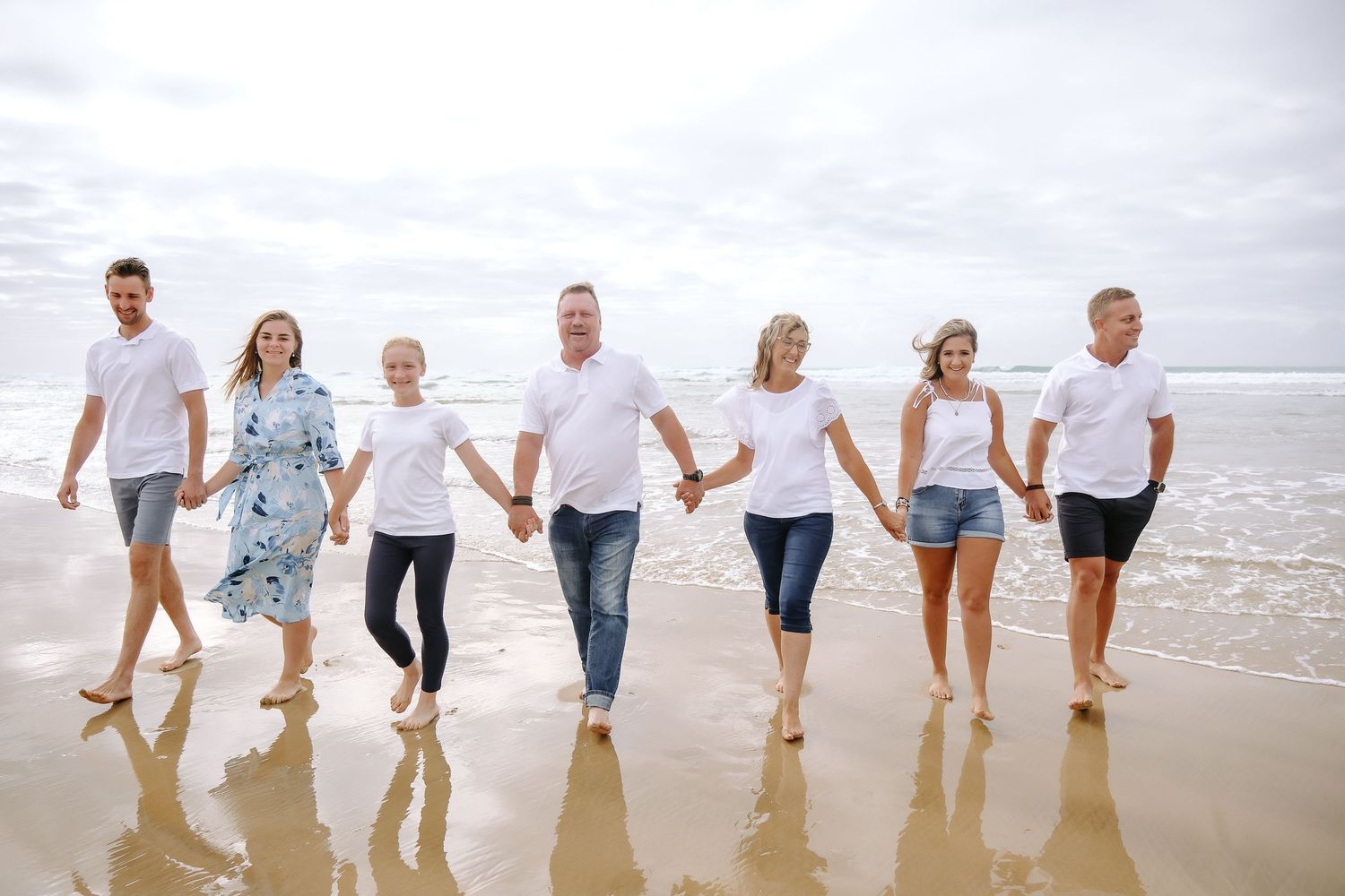 Group walking together holding hands along the beach shoreline.