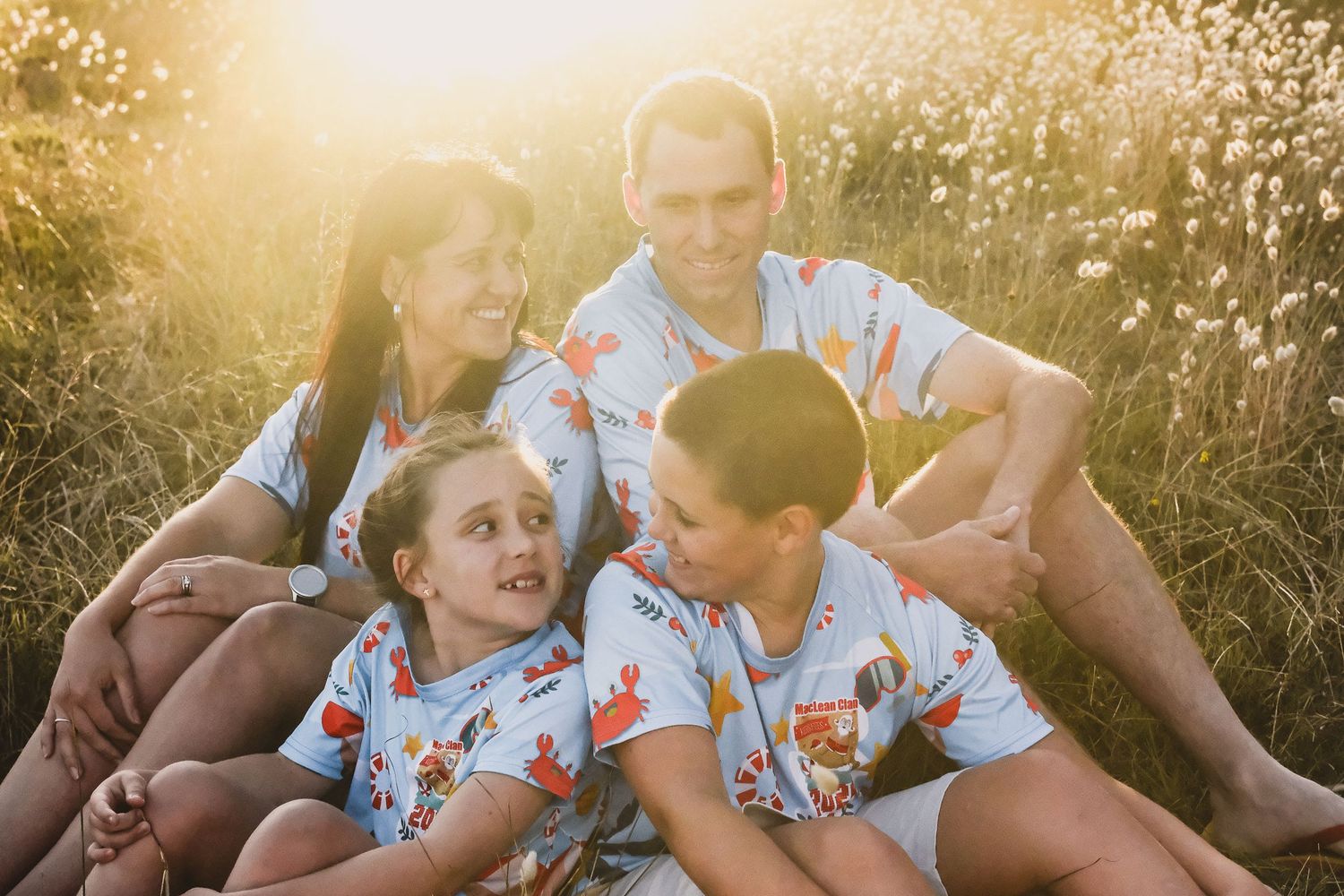A family group wearing matching floral shirts sits together in a sunny field.