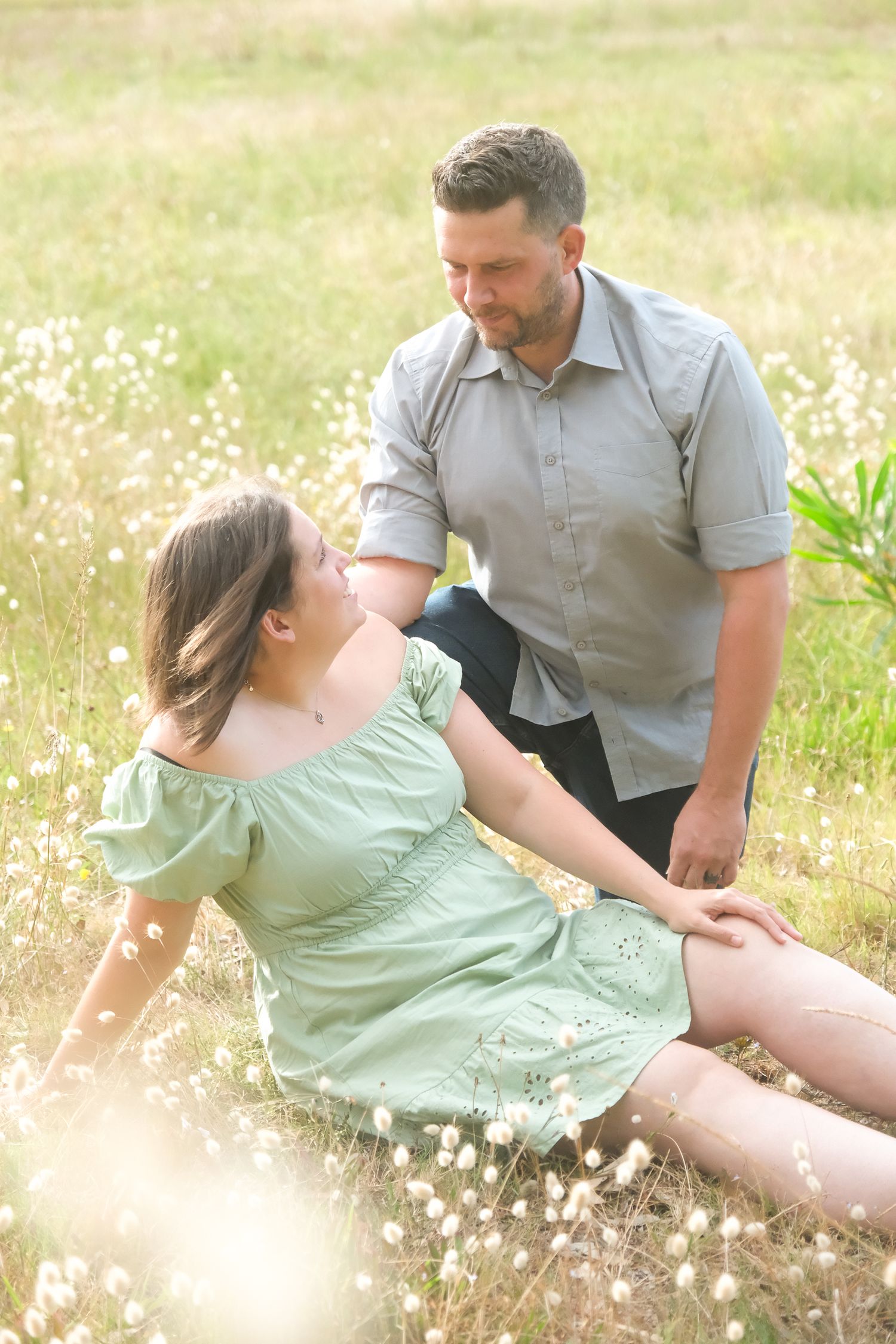 A couple shares an intimate moment in a sunlit field of wildflowers.