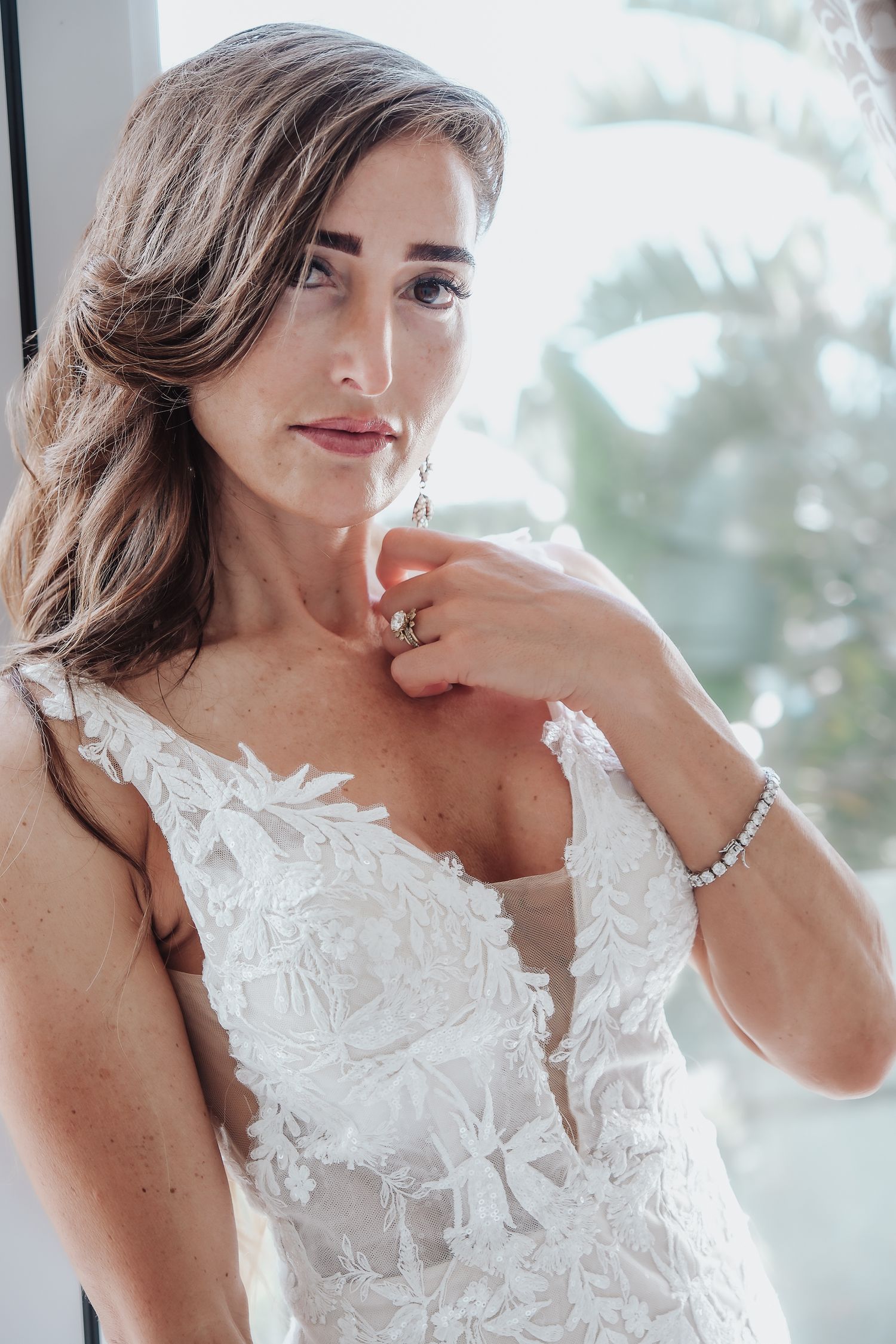Close-up of bride in intricate white lace wedding gown with delicate jewelry.