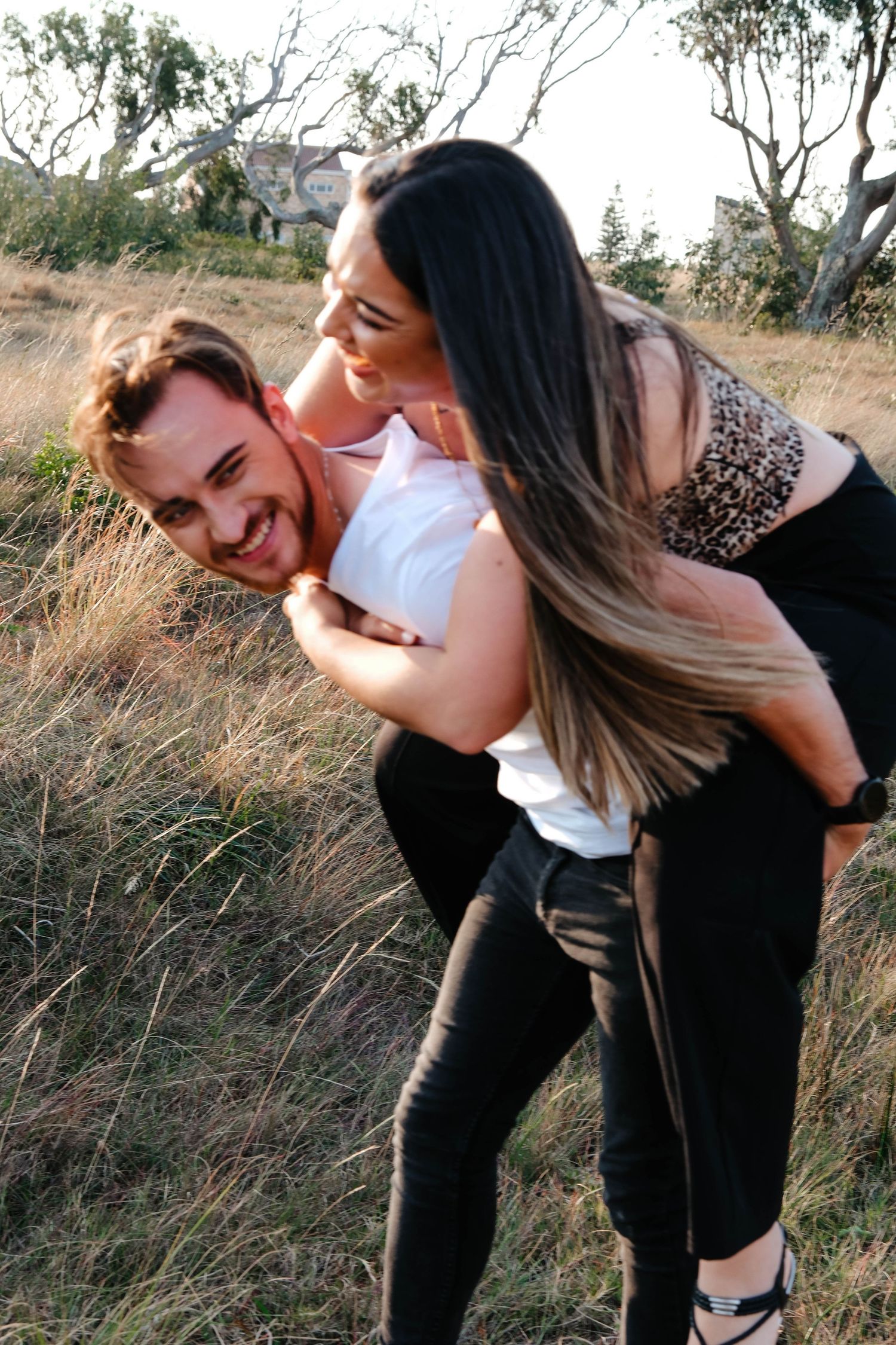 A playful piggyback ride moment captured in a grassy outdoor setting.