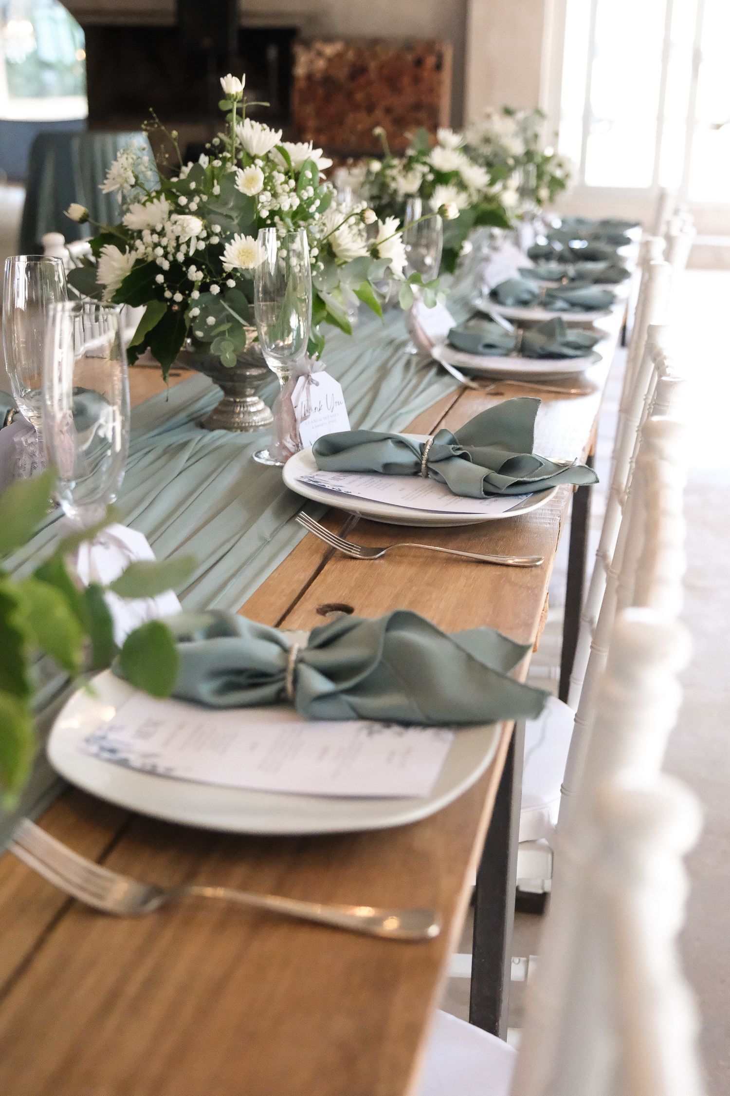 Elegant wedding table setting with sage green napkins and white floral centerpieces.