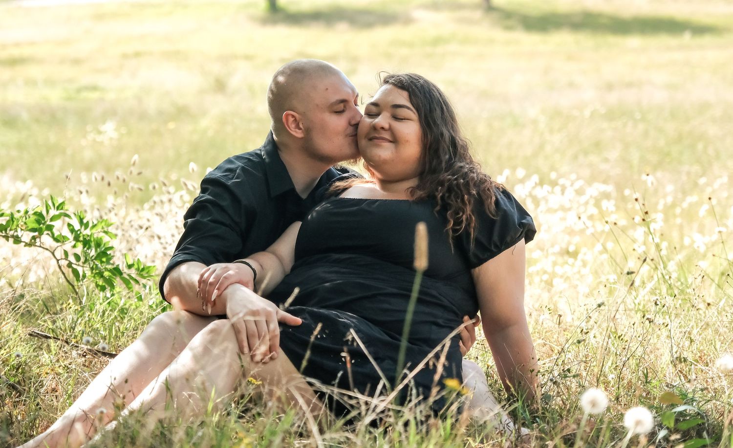 A loving couple laughing together while sitting in a sunny meadow with wildflowers.