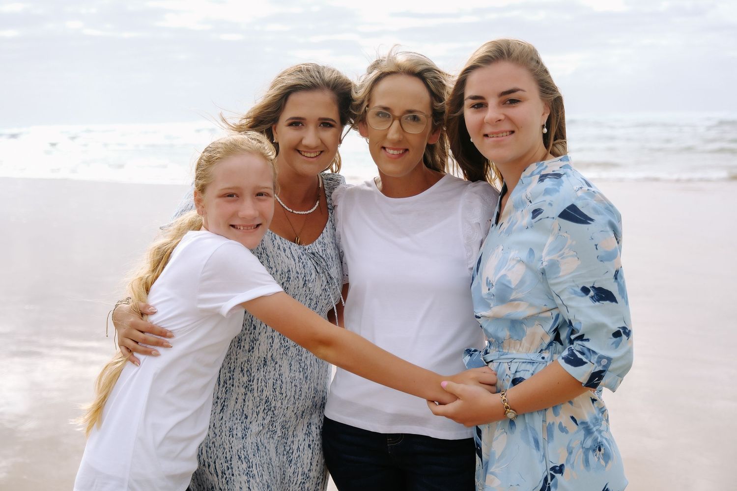 Four people embrace while posing for a photo on a cloudy beach.
