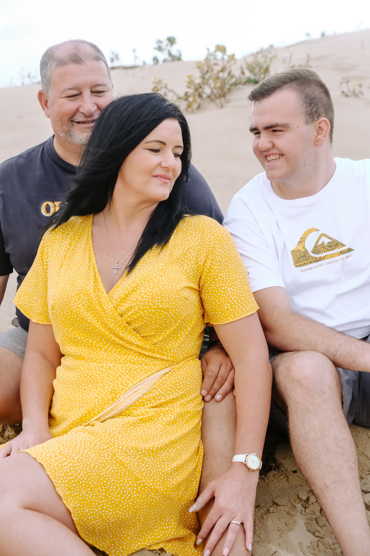 Three people sitting together outdoors, with one wearing a bright yellow dress.