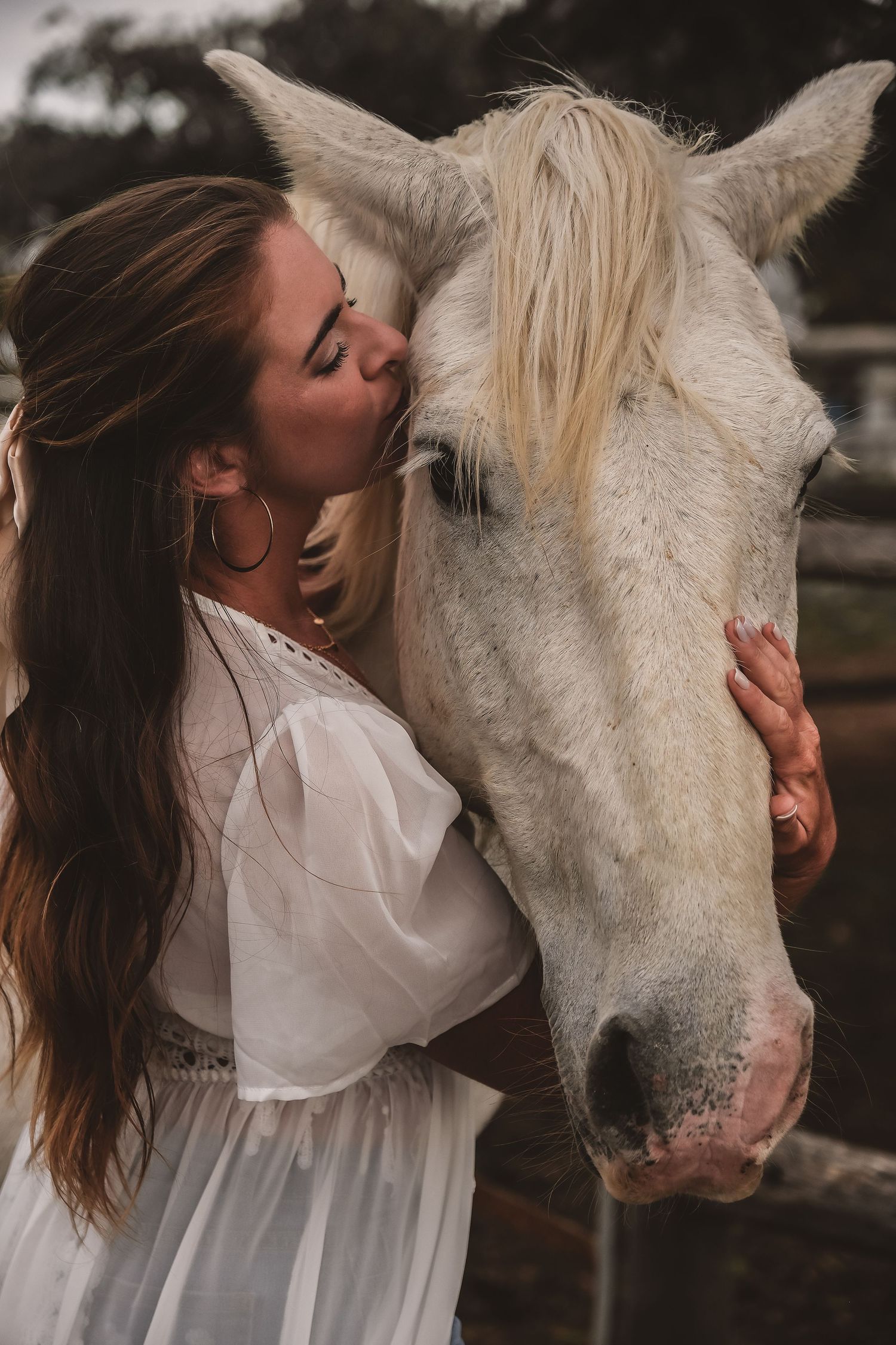 A tender moment between a woman in white dress and a white horse.