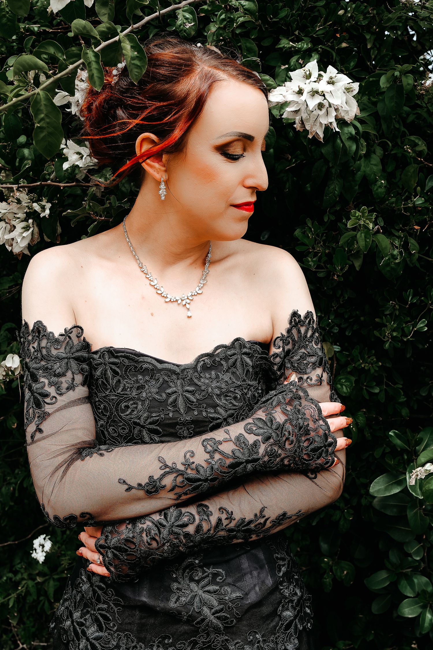 A formal portrait featuring a black lace dress against flowering bushes.