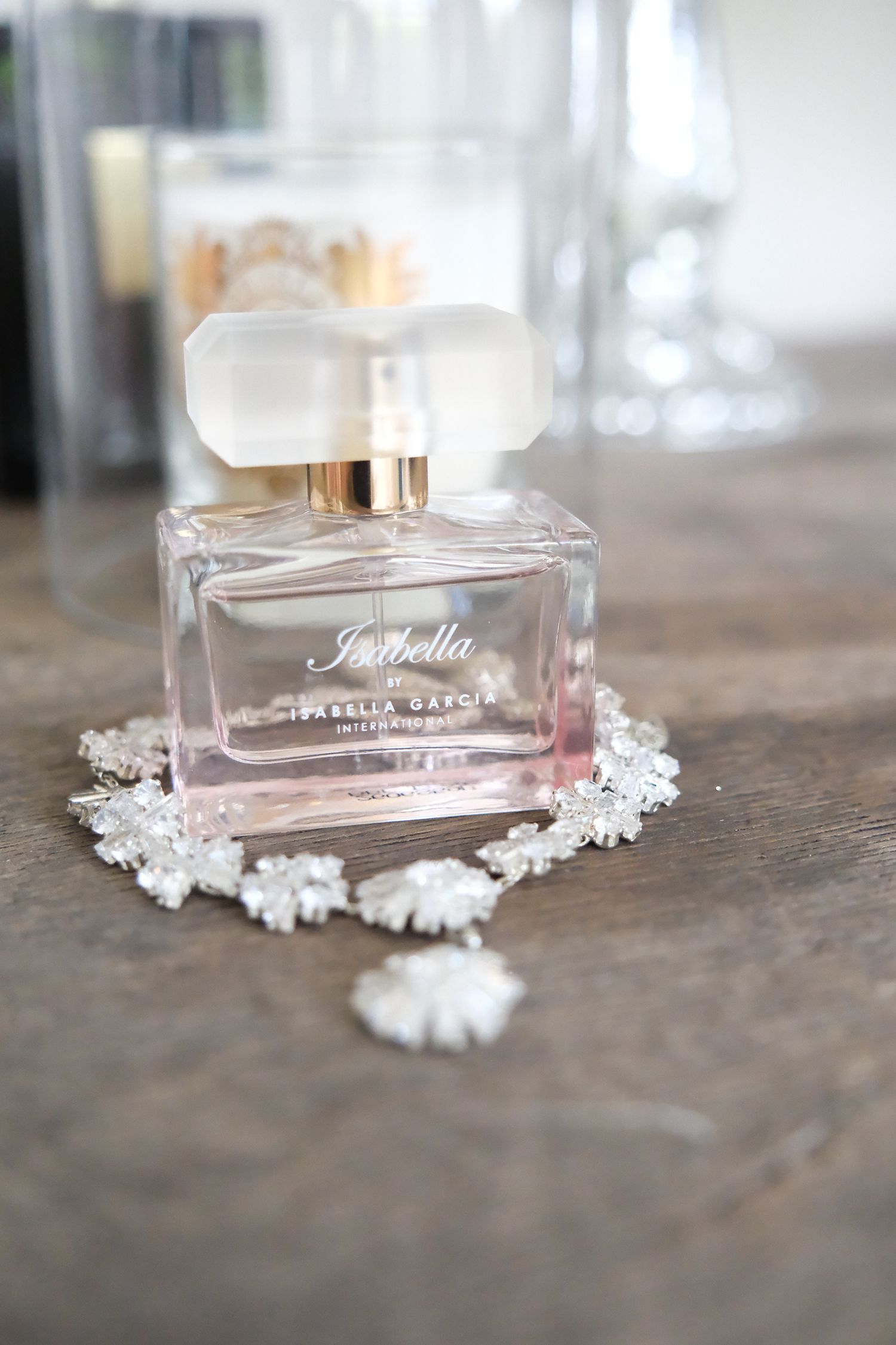 A pink perfume bottle labeled 'Isabella' surrounded by delicate white decorative elements on a wooden surface.