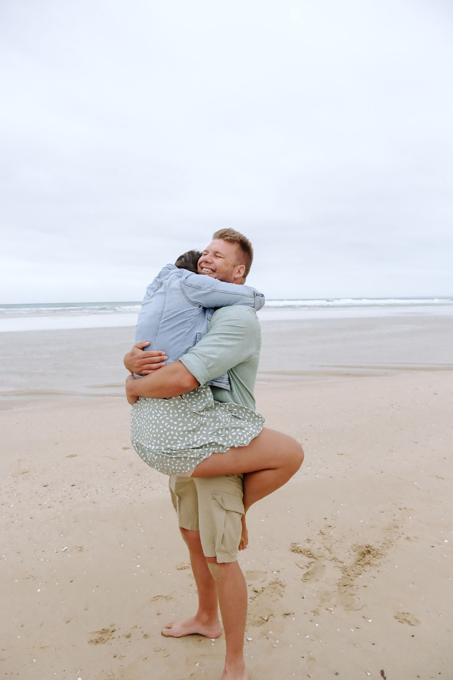 Joyful lift and embrace on cloudy beach shore.