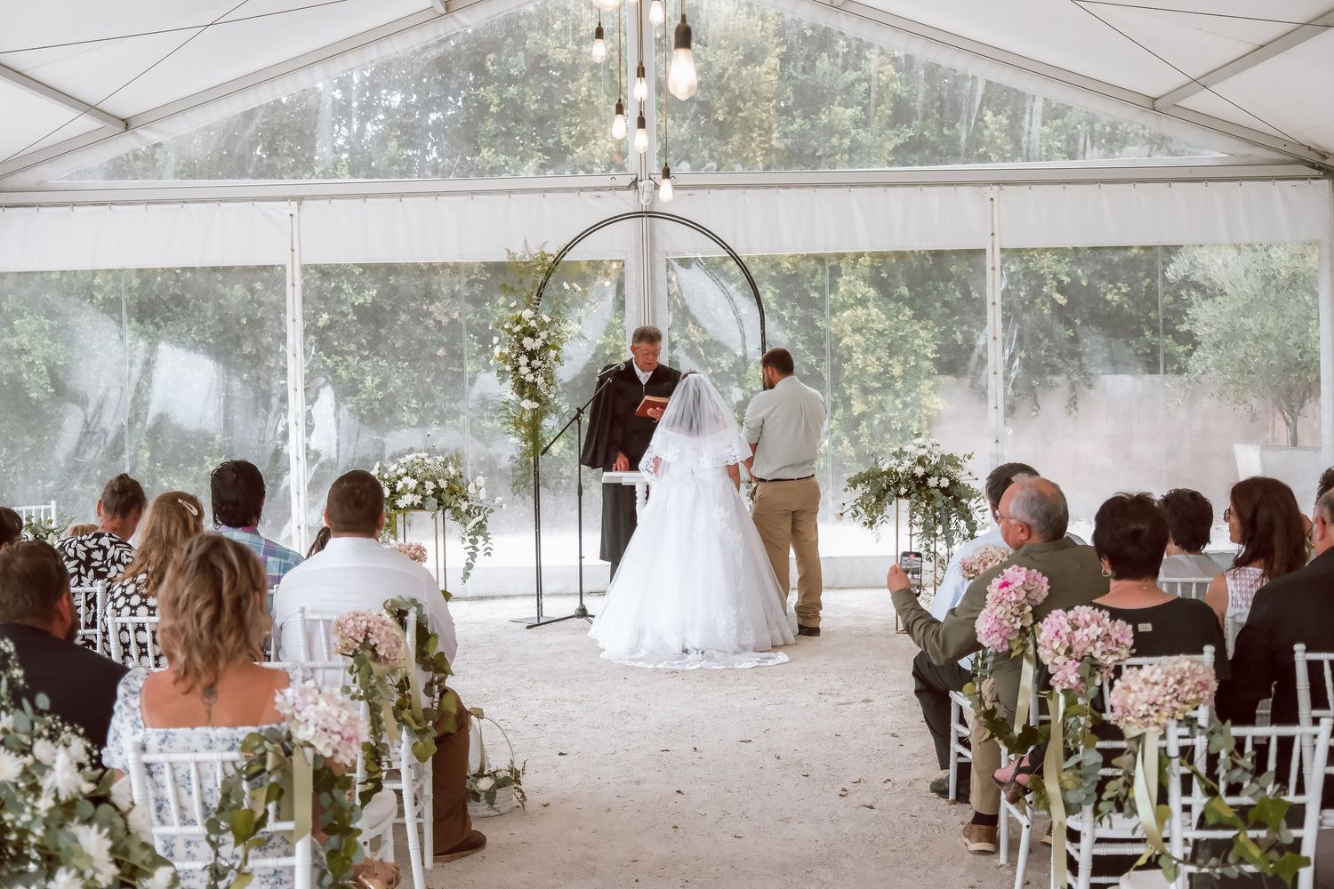 Wedding ceremony in white tent with floral arch and guest seating.