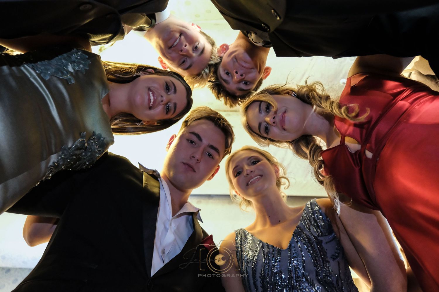 Group forms a circle looking down at the camera from above while hugging together.