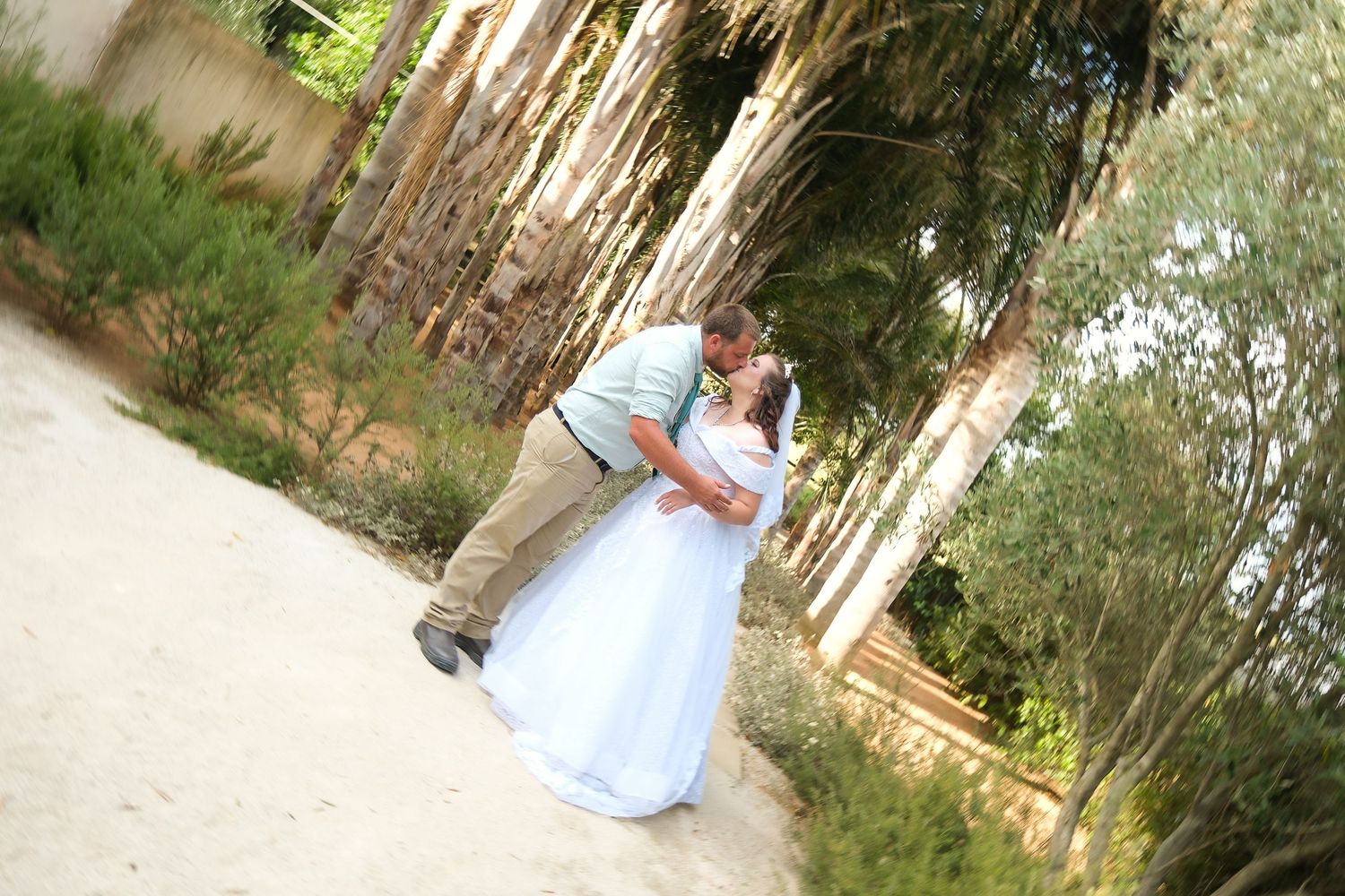 A romantic wedding couple shares an intimate moment in a woodland path setting.