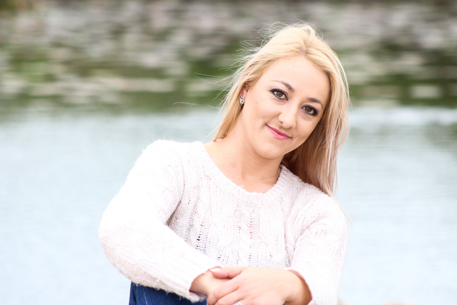 Outdoor portrait by a lake wearing a cozy white sweater.