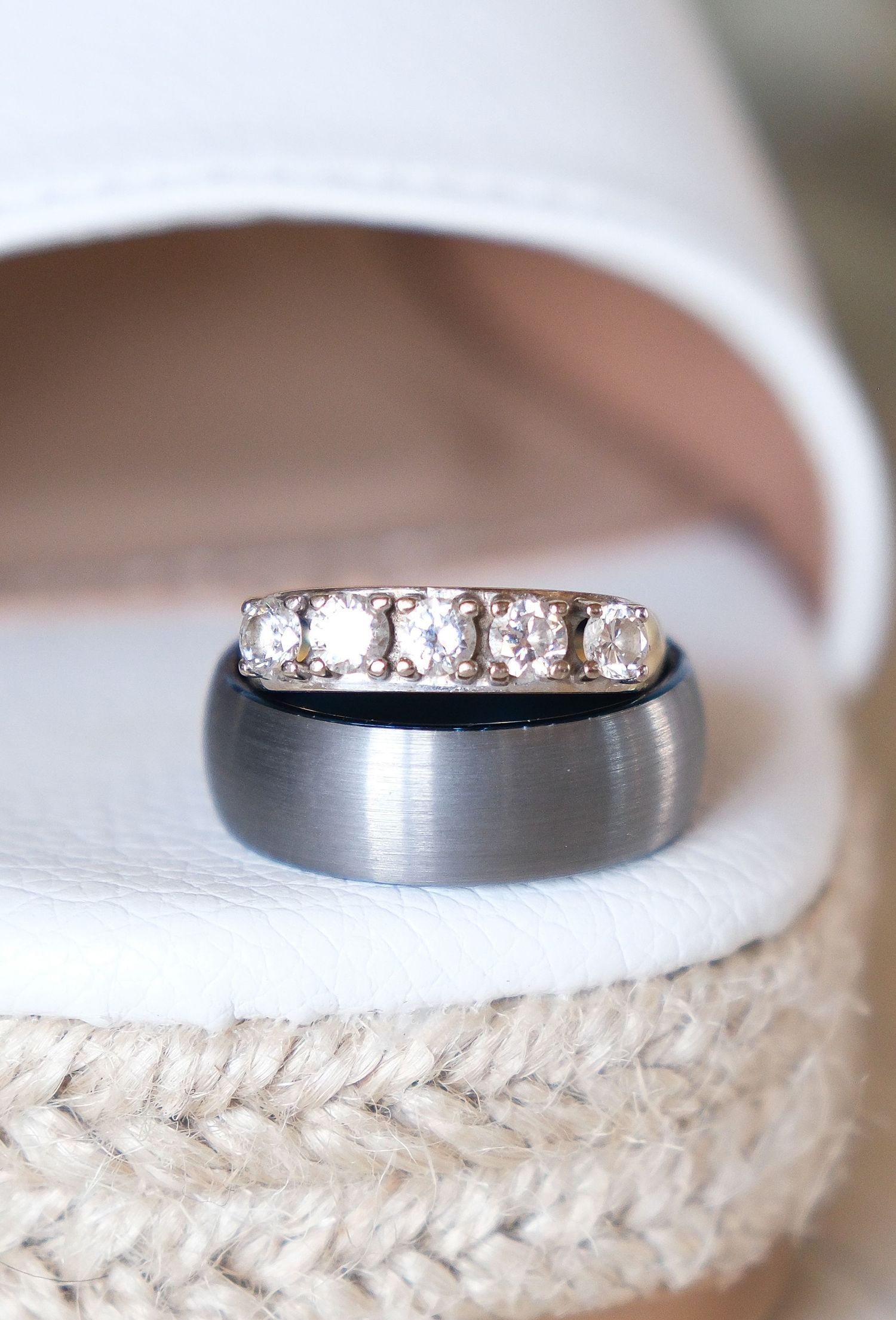 Close-up of wedding rings showing a diamond band and brushed metal band on textured fabric.