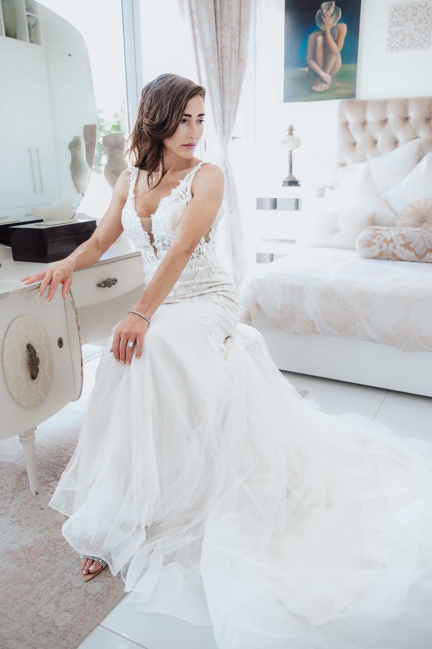Elegant white lace wedding dress shown in a luxurious bedroom setting.