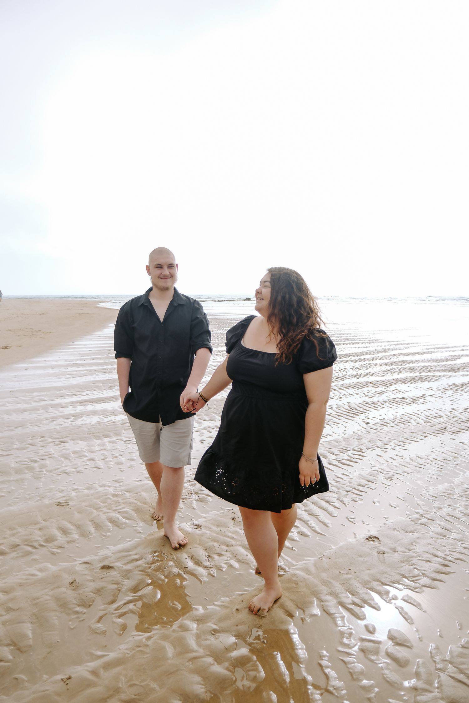 A couple walking hand in hand along a peaceful beach at sunset.