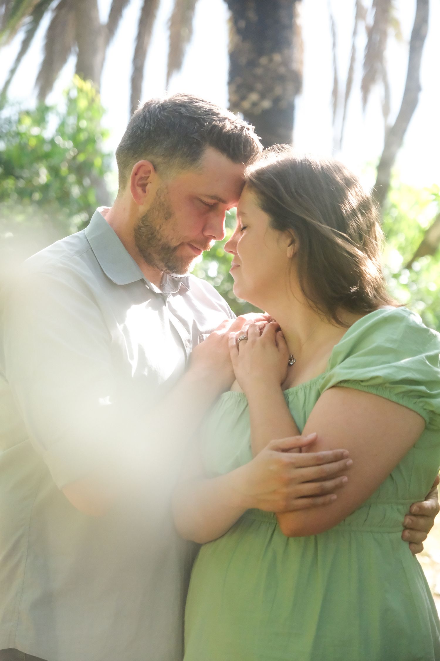 Intimate portrait of couple in soft lighting with greenery backdrop.