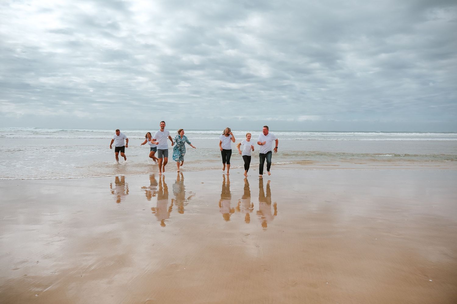Group of people walking and playing together on a reflective beach shore during overcast weather.