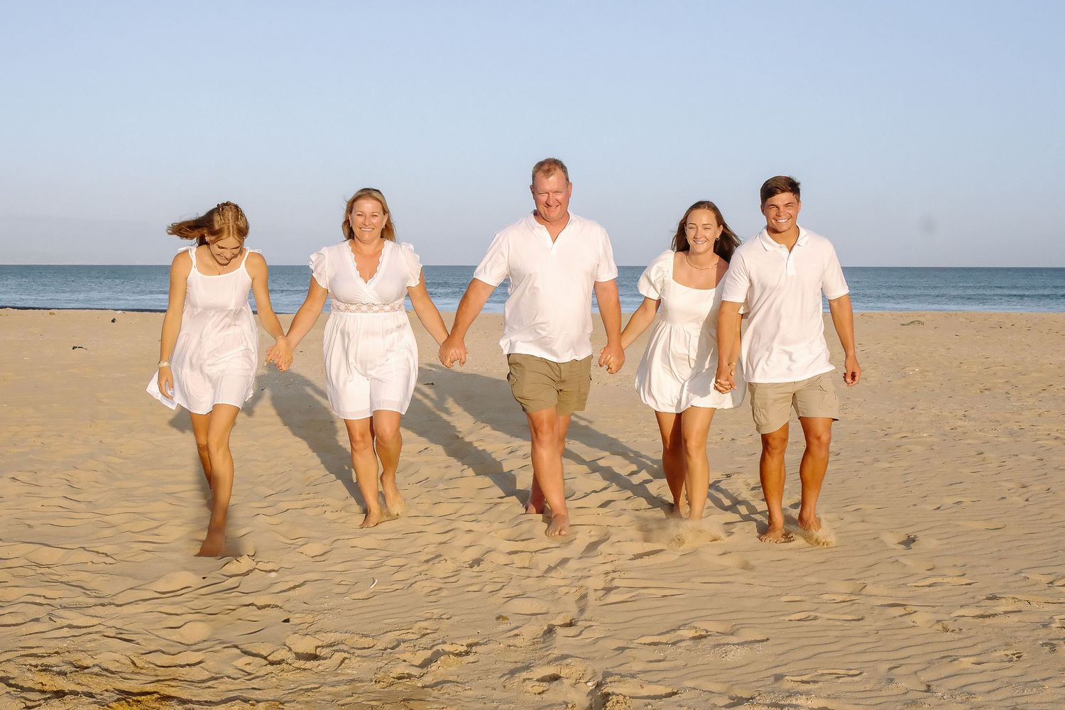 A group walking together along the beach wearing coordinated white summer outfits.