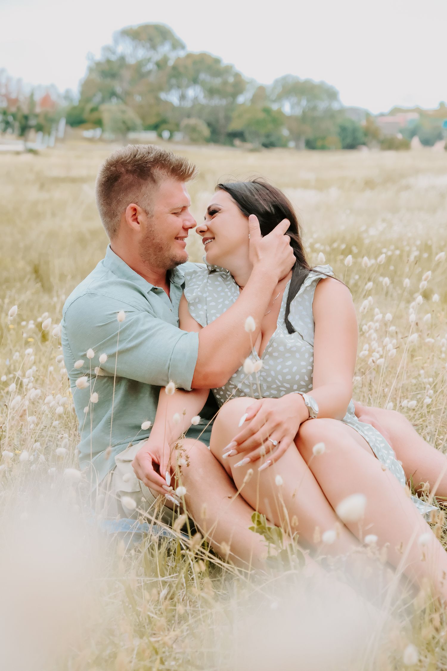 A romantic couple sitting together in a sunlit field of wildflowers.