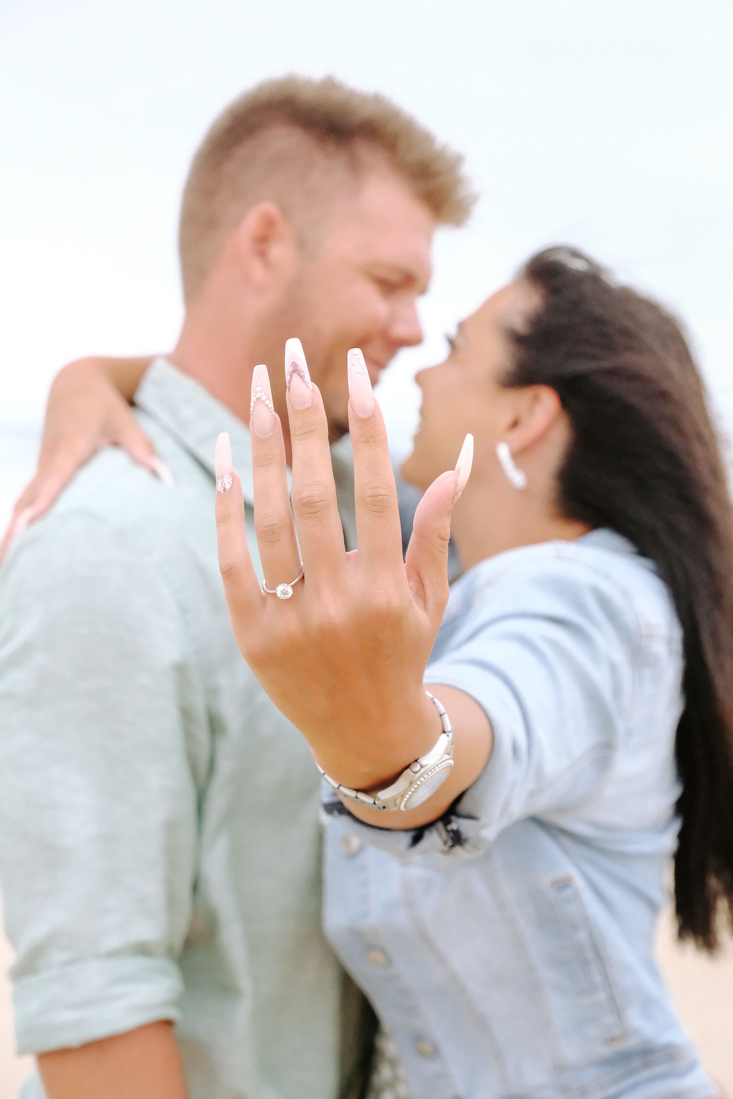 A newly engaged couple embracing while showing off the engagement ring on the beach.